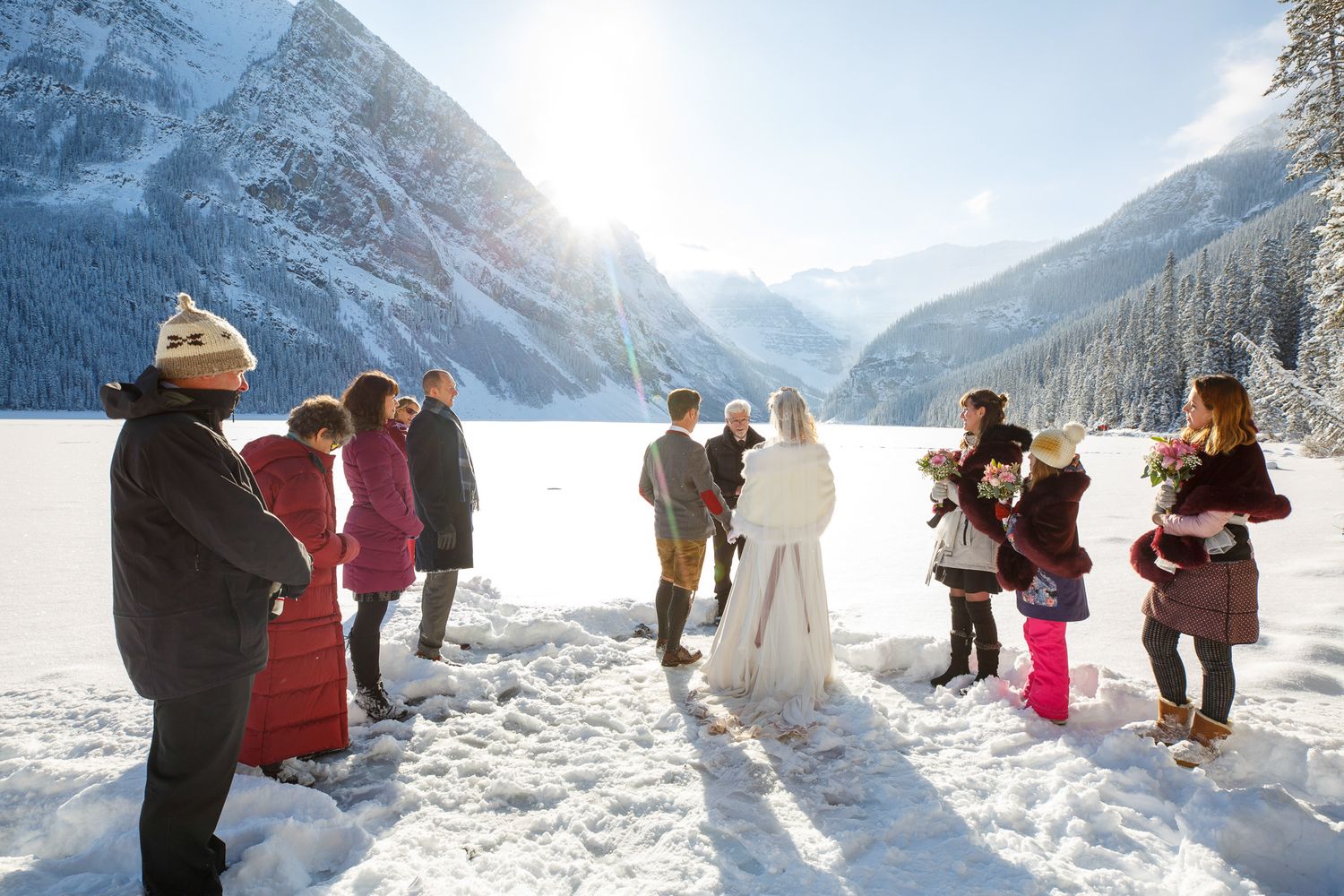 A group of people enjoying a winter wedding ceremony in the snowy mountains with dramatic mountain peaks in the background at Lake Louise.