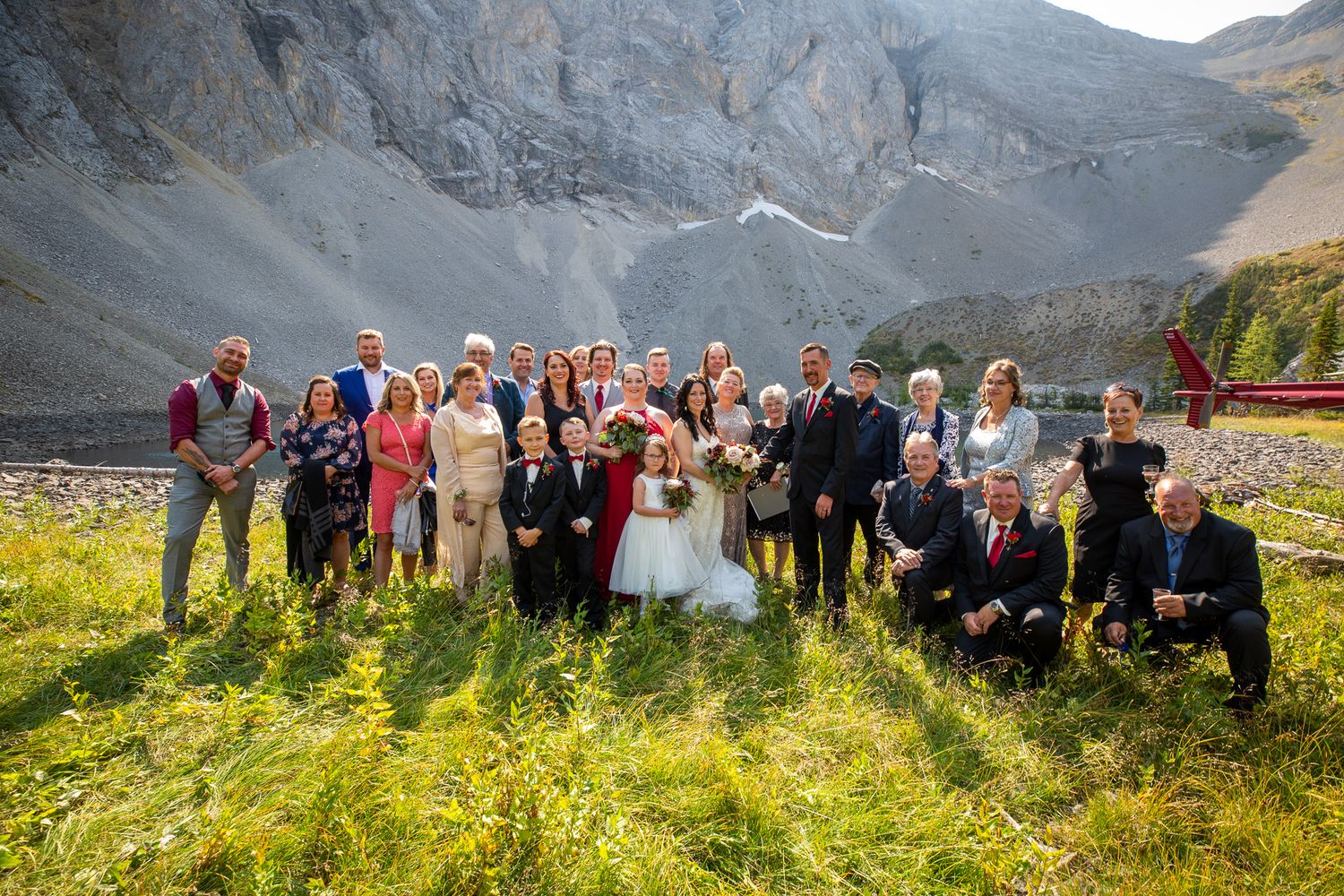 Wedding party poses outdoors in mountain landscape with glacier backdrop on sunny day in Kananaskis, Alberta.