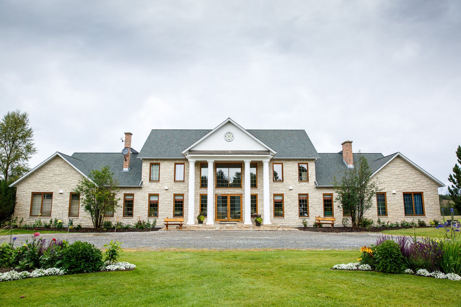 Grand neoclassical estate with white columns, manicured gardens, and lush green lawns under overcast skies at Cherry creek estate Kimberley
