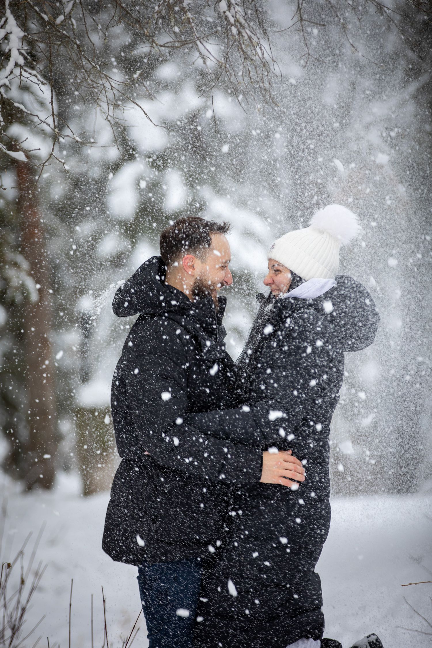 A couple shares a tender winter moment in falling snow while wearing warm coats and winter attire. Vermilion lakes in Banff. AB