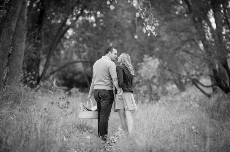 Black and white photo of a couple kissing in a lush forest meadow, surrounded by tall trees and grasses at Fish Creek Park in Calgary.