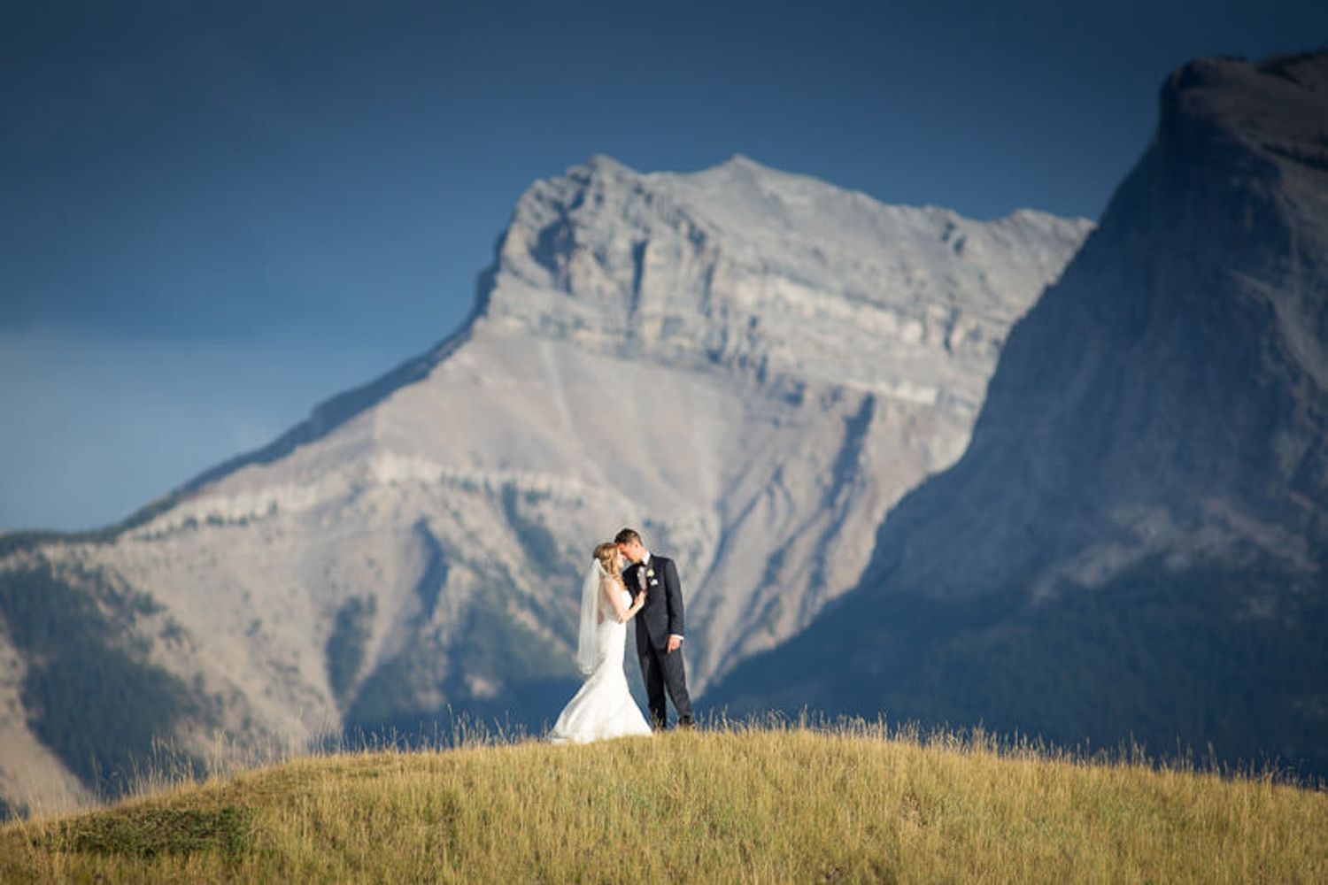 A wedding couple poses in front of majestic snow-capped mountains in Banff National Park during their outdoor ceremony. Canmore Three Sister