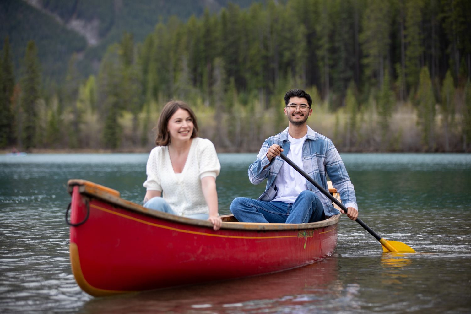 A couple enjoys a peaceful afternoon paddling their red canoe across a scenic mountain Reservoir lake in Canmore, Alberta