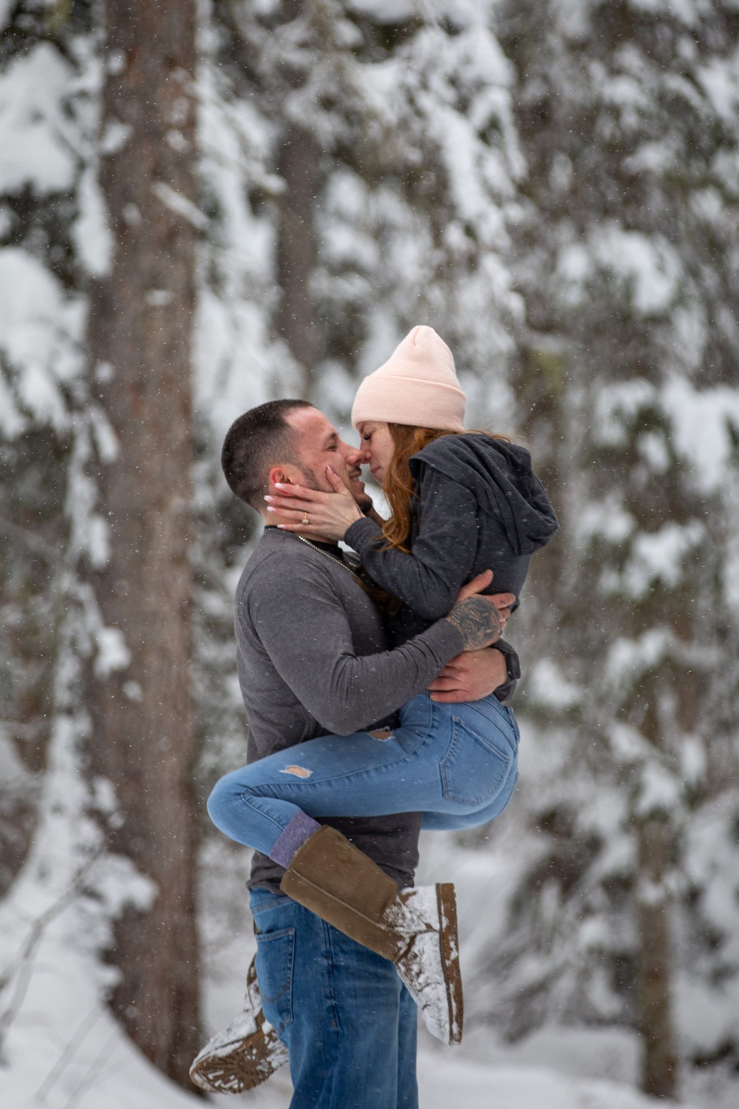 A couple embraces in a romantic moment against a snowy forest backdrop during a winter photo session at Emerald Lake Lodge, in BC.
