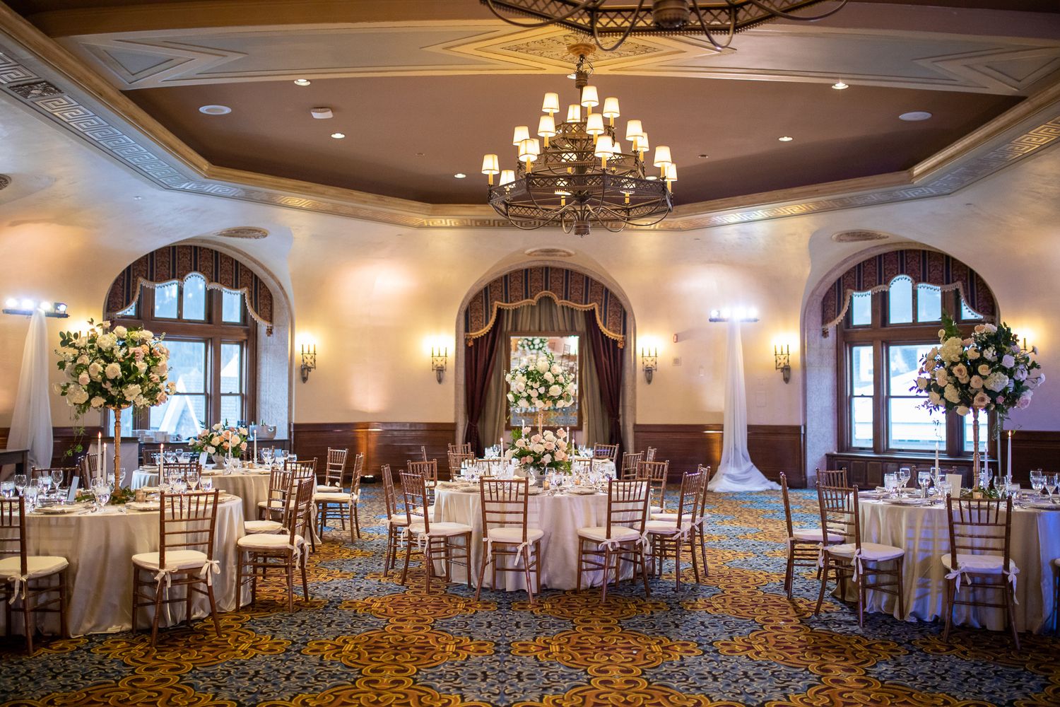 Alhambra ballroom with arched windows, crystal chandelier, and round tables set for a formal wedding reception at Fairmont Banff Springs.