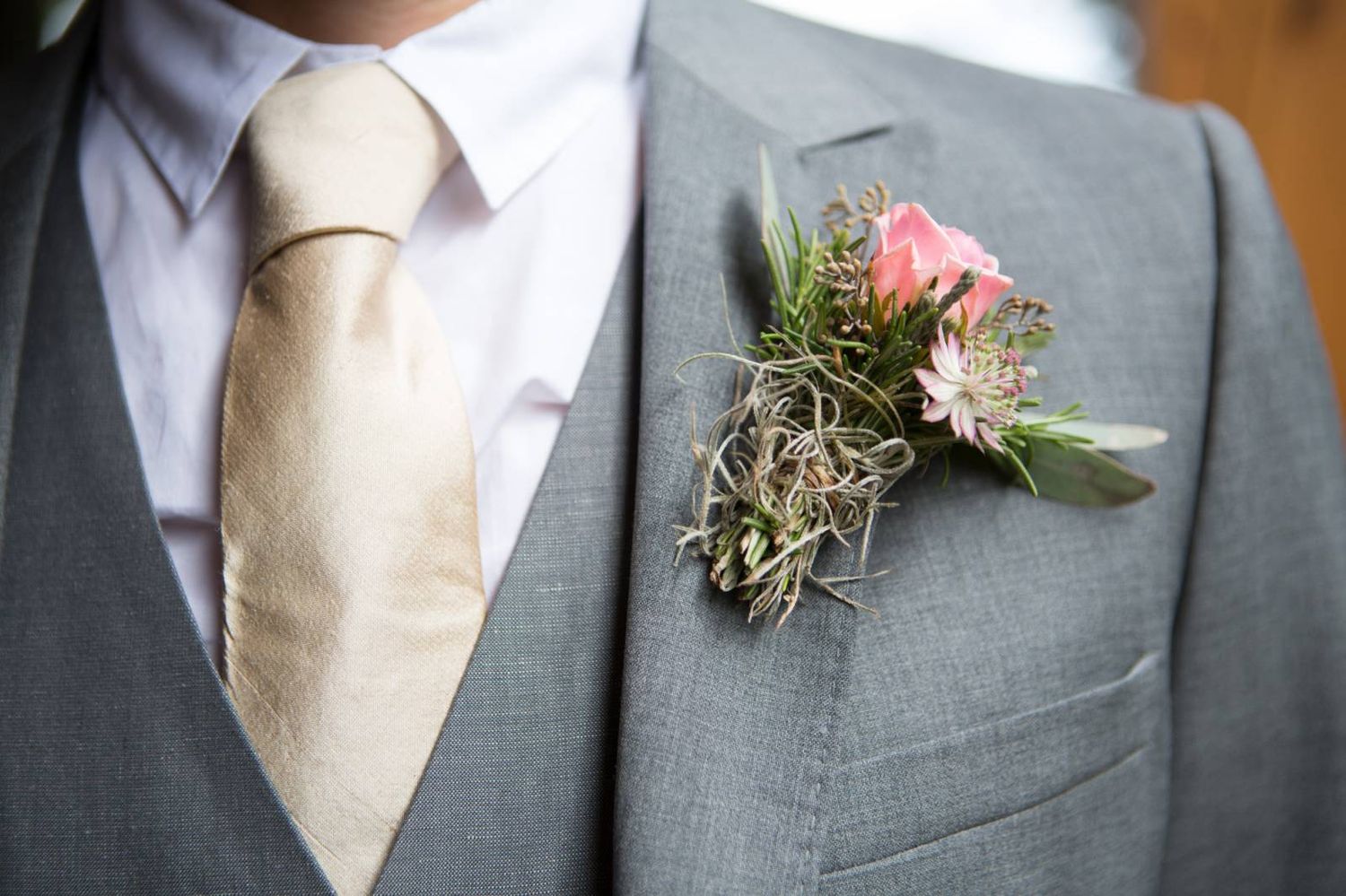 Groom with a wedding boutonnieres with white and pink flowers pinned to grey suit lapels at Buffalo Lodge in Banff, Alberta