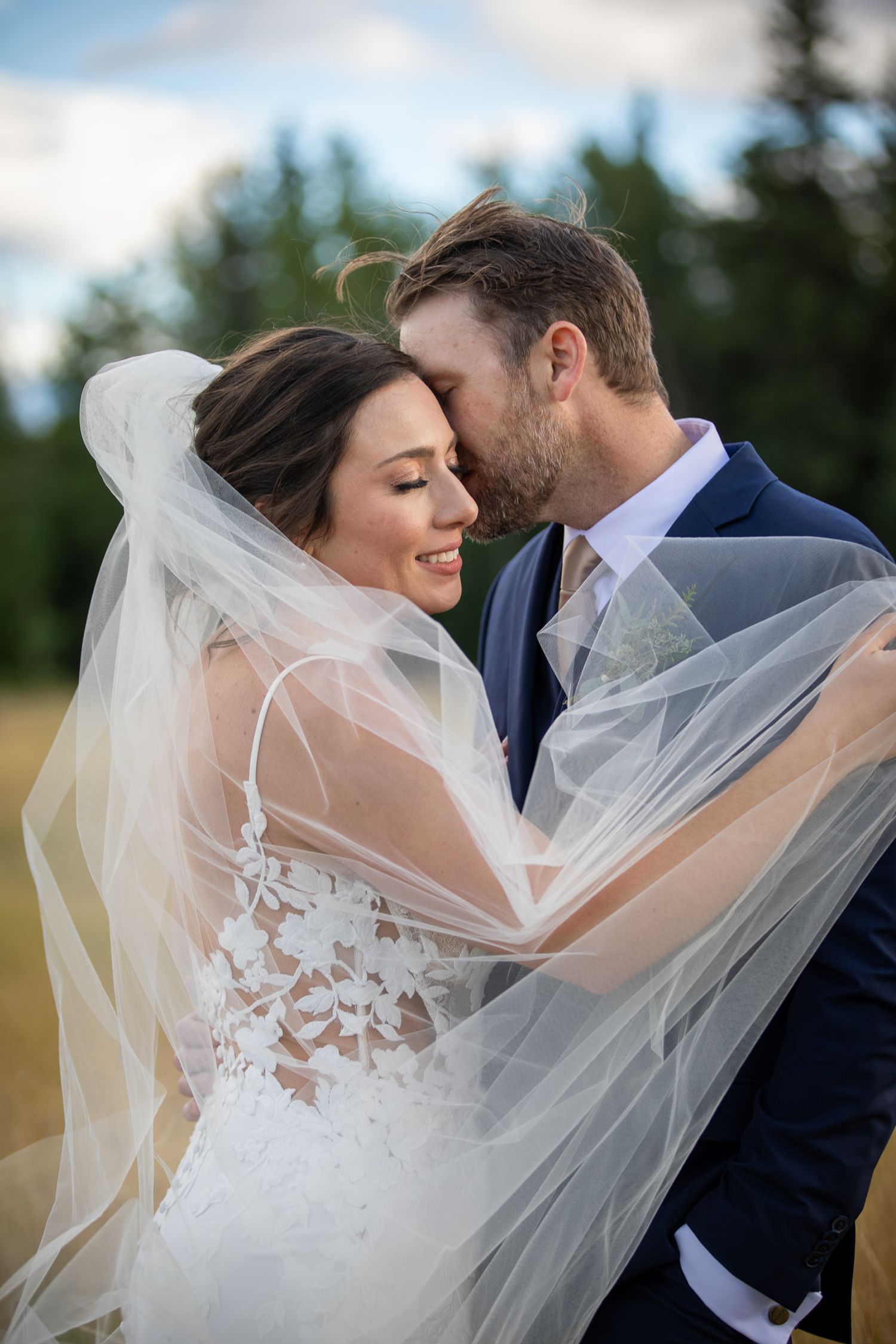 A romantic wedding couple embraces outdoors as the bride's delicate veil flows in the breeze. Banff, Alberta