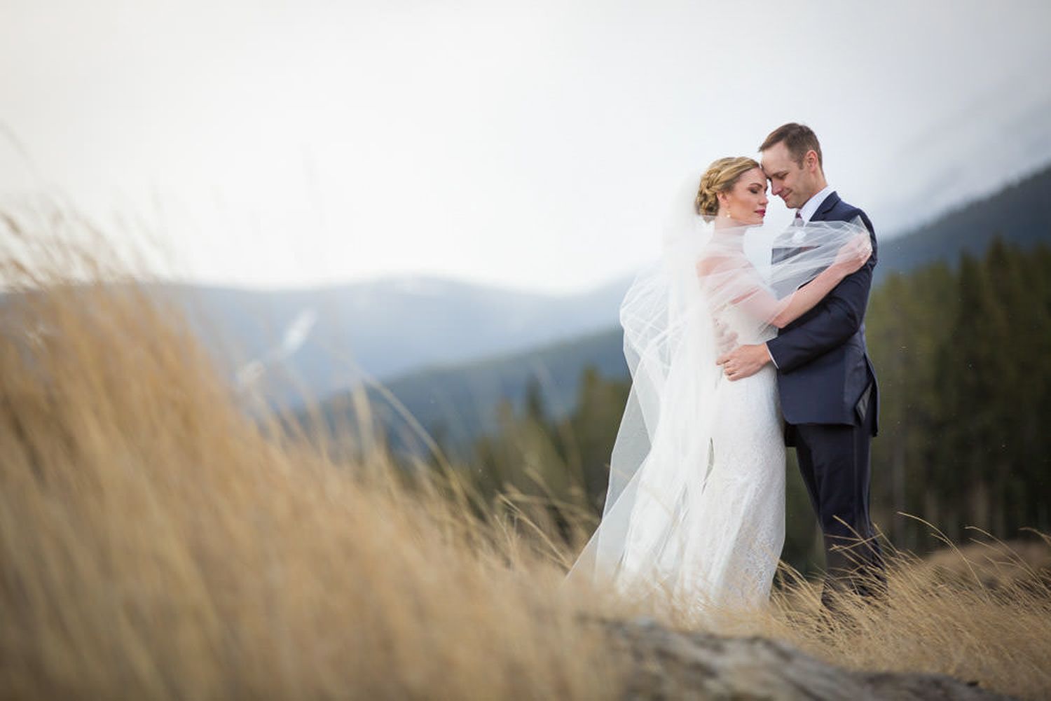 A couple in wedding attire embraces in a misty mountain landscape during their romantic outdoor ceremony. Canmore Alberta.