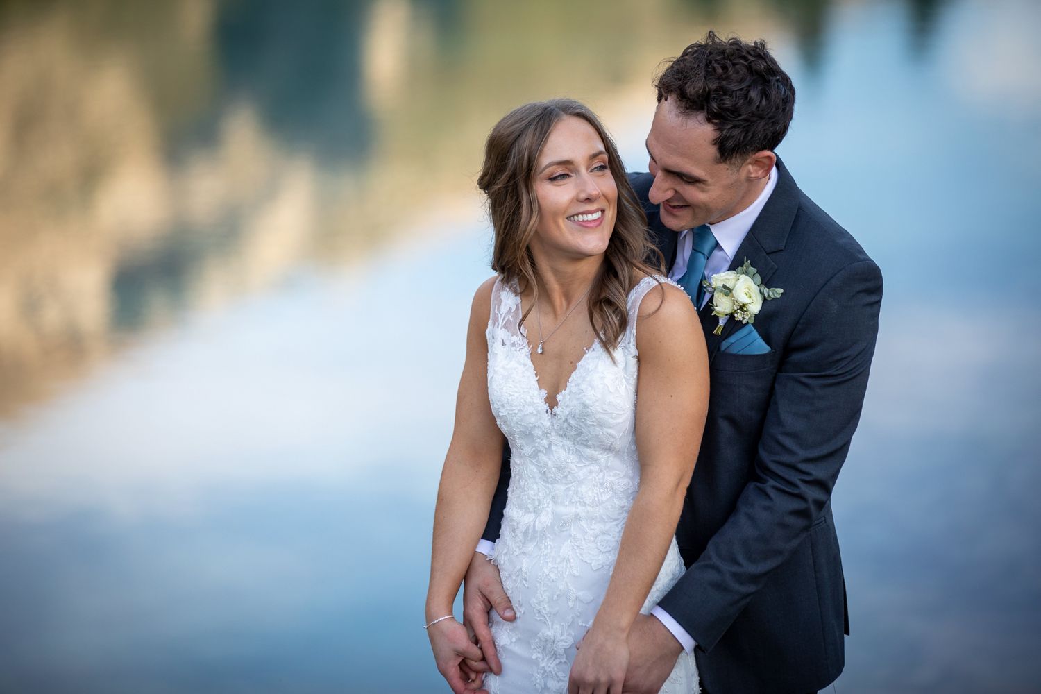 A romantic wedding photos showing a couple embracing and laughing together by the water at sunset. Silvertip Resort, Canmore, Alberta.