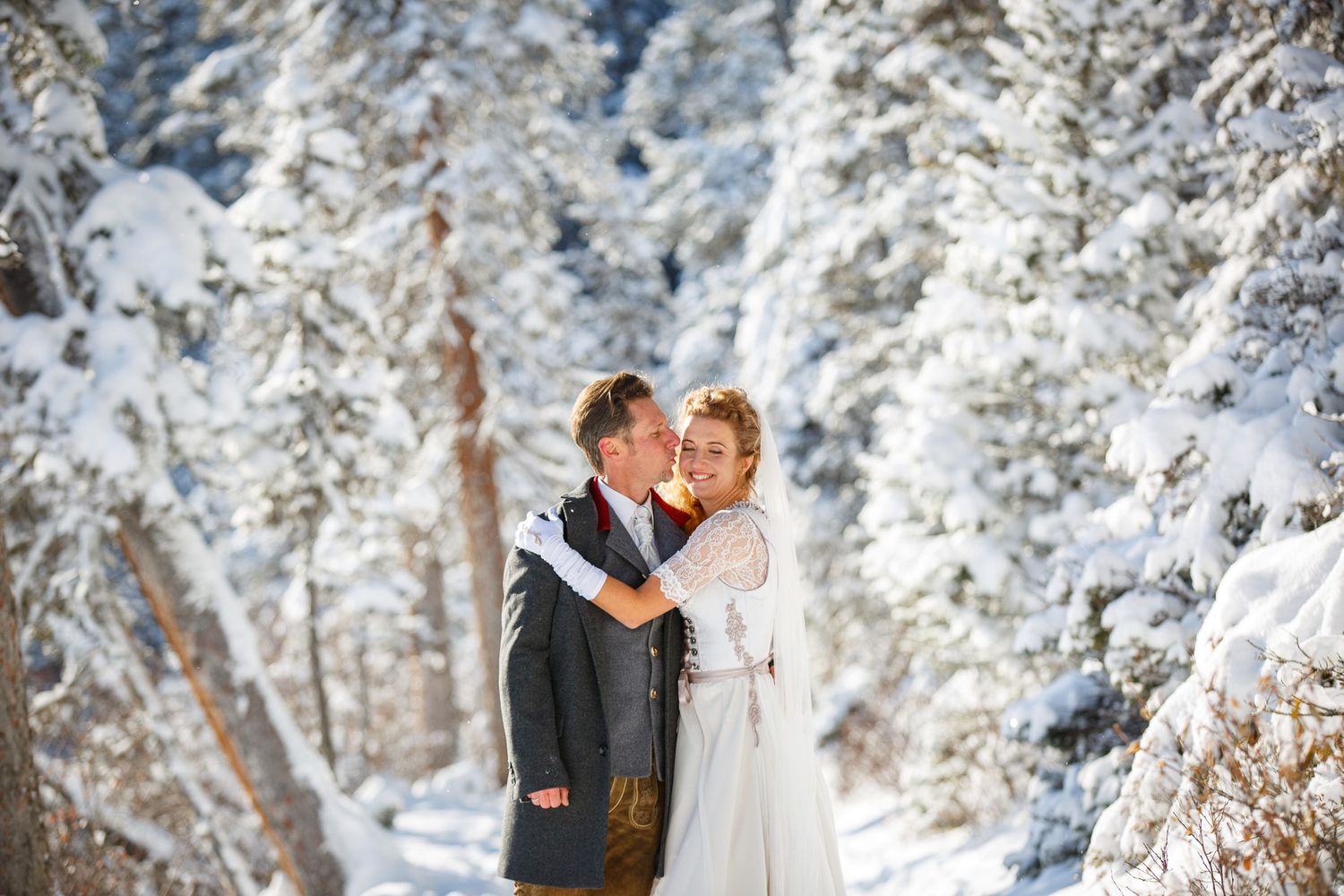 A couple embraces in a snowy winter forest setting with snow-covered evergreen trees creating a magical backdrop at lake Louise, Alberta.