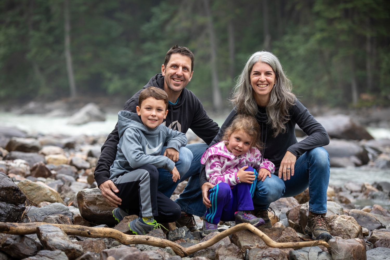Family enjoying time together on a rocky beach surrounded by evergreen forest and rushing Toby creek river in Panorama, BC