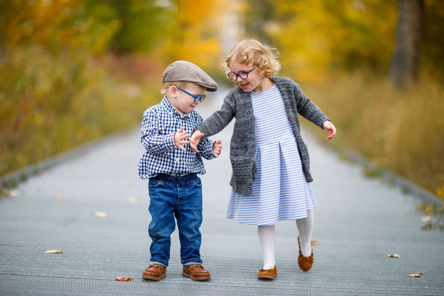Two pairs of small feet in jeans and white shoes walking together on a leaf-covered path during autumn at Calgary Zoo.
