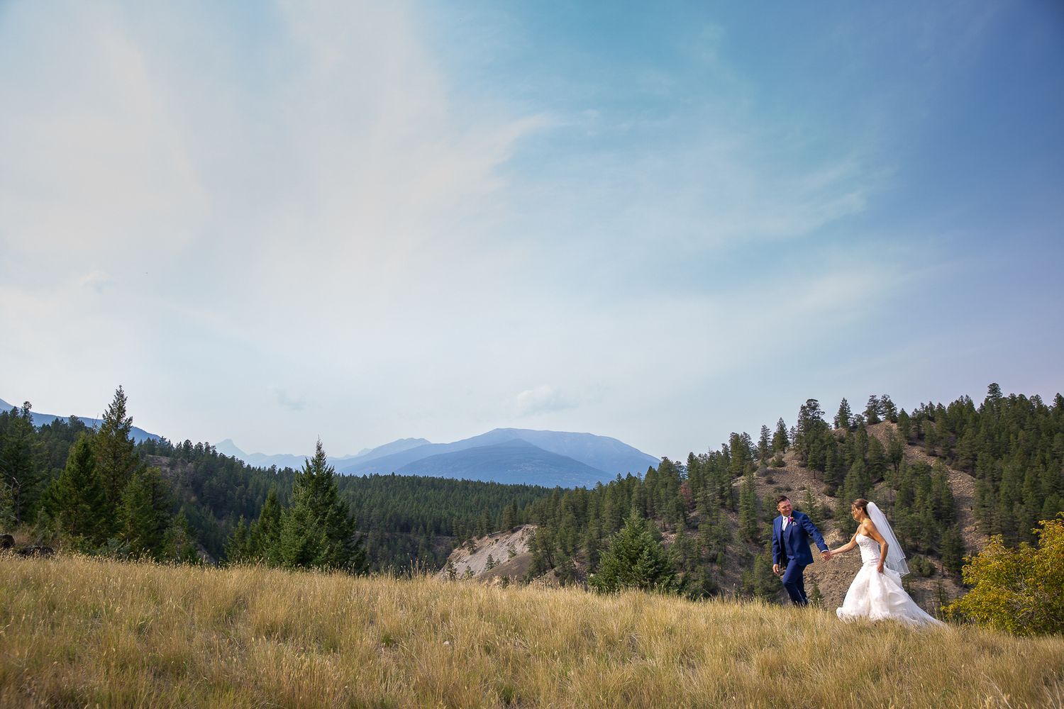 Wedding couple walking on a mountain ridge with Mount Neilson in the background in Invermere, British Columbia.