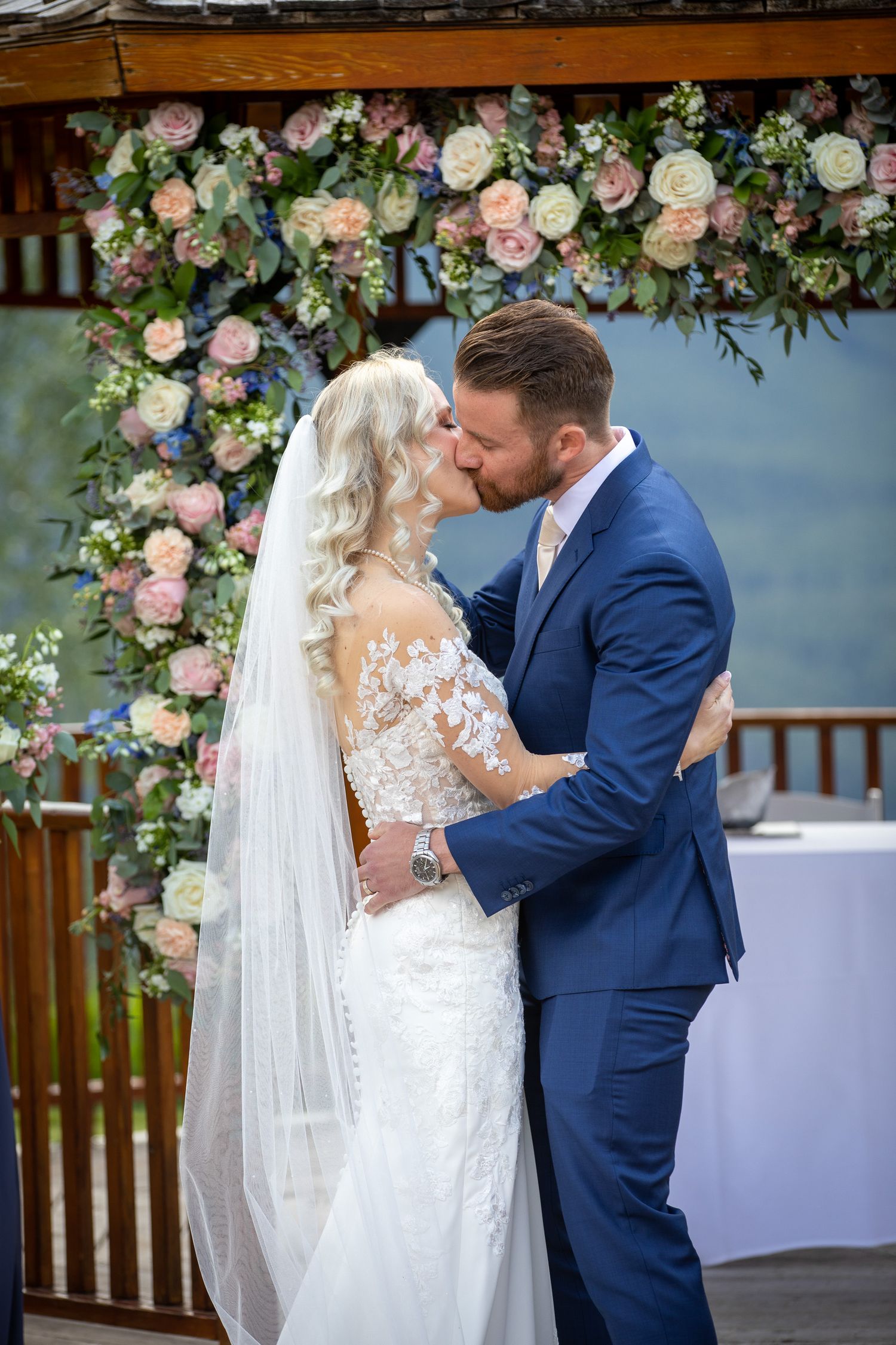 Bride and groom share first kiss at outdoor wedding altar adorned with pink and white floral arrangements at Silvertip gazebo in Canmore.
