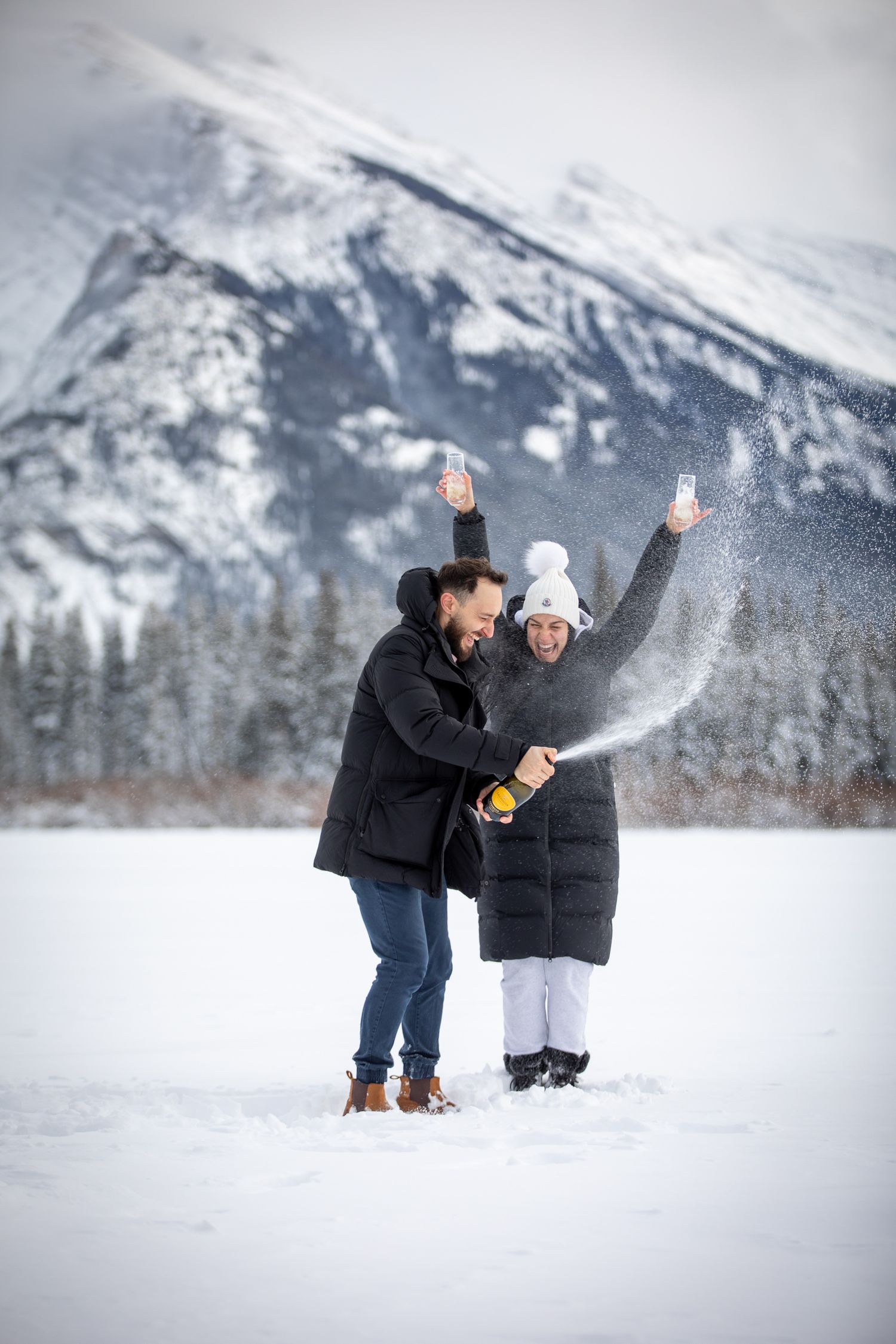A couple plays in the snow against a backdrop of snowy mountains Mount Rundle in winter in Banff.