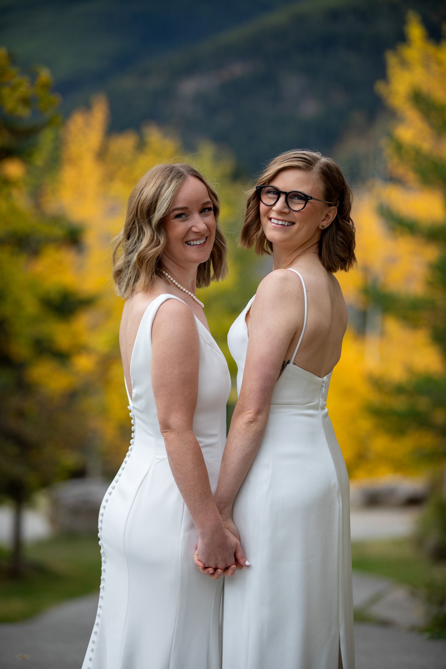 A LGBTQ couple in white dresses share a joyful moment together against a backdrop of autumn foliage. Panorama Mountain Resort.