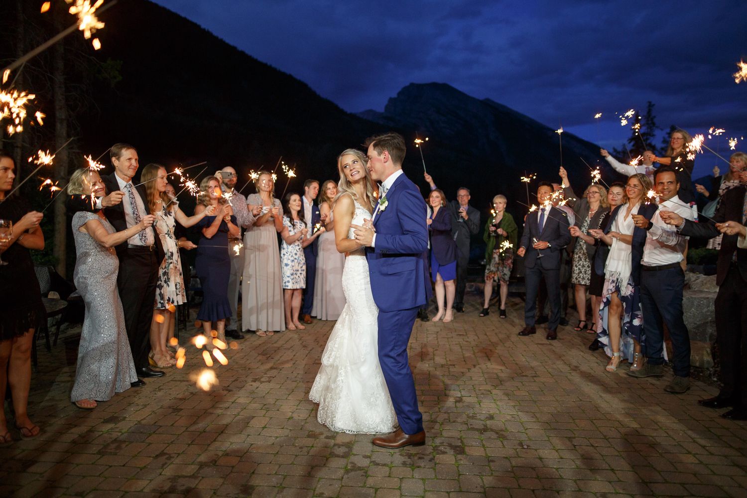 Wedding guests hold sparklers in a line creating a magical nighttime tunnel on the beach for the newlyweds. Silvertip resort in Canmore.