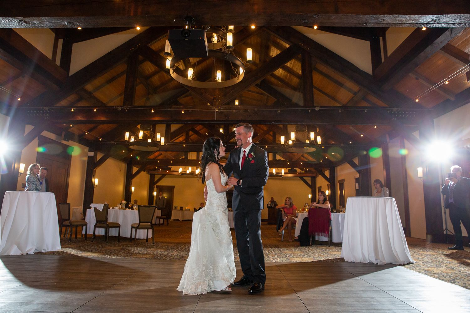 Bride and groom share their first dance in an elegant rustic barn wedding venue with wood beamed ceilings and warm lighting at Silvertip.