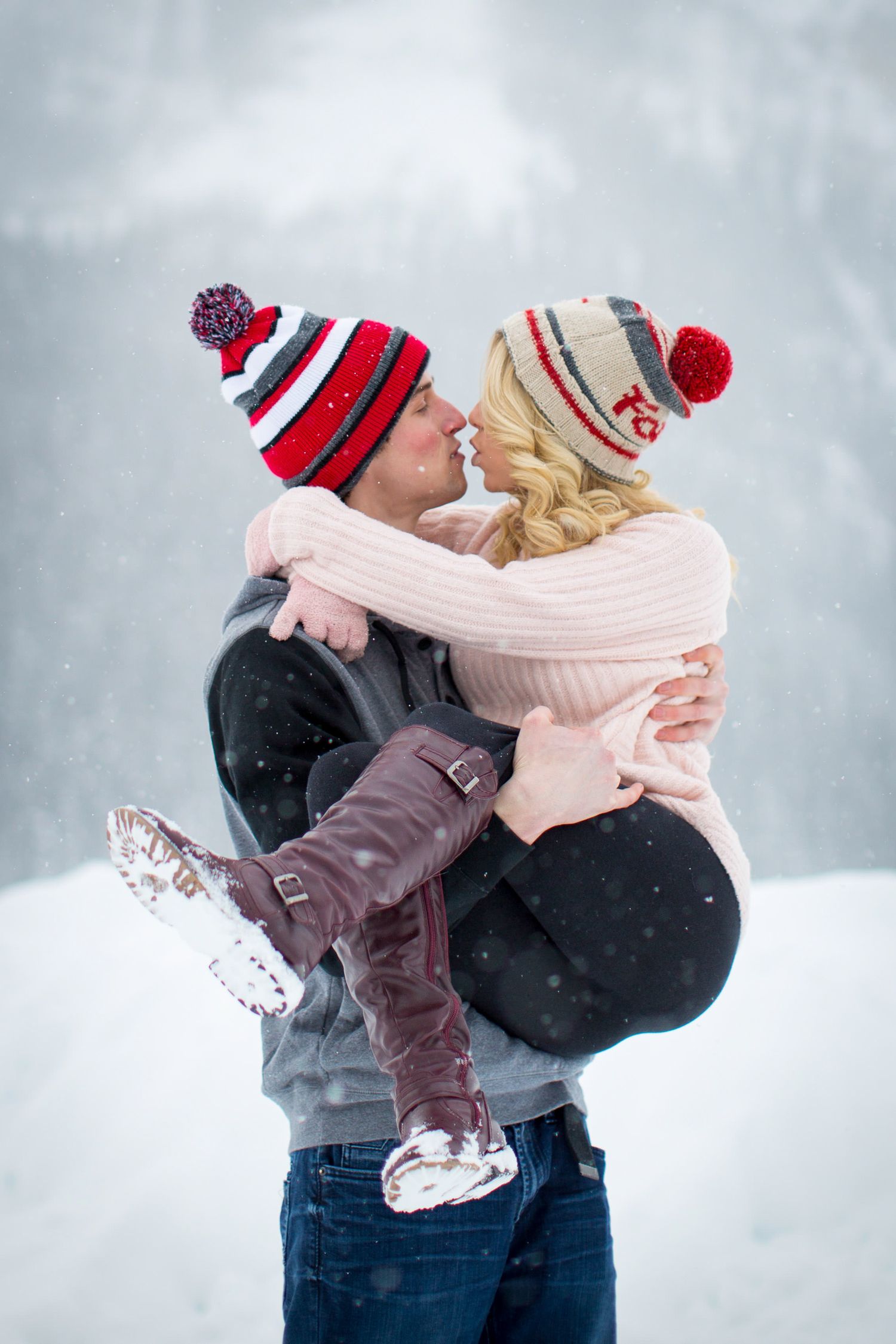 A romantic winter embrace between a couple wearing cozy knit hats and sweaters in the falling snow at Lake Louise, AB