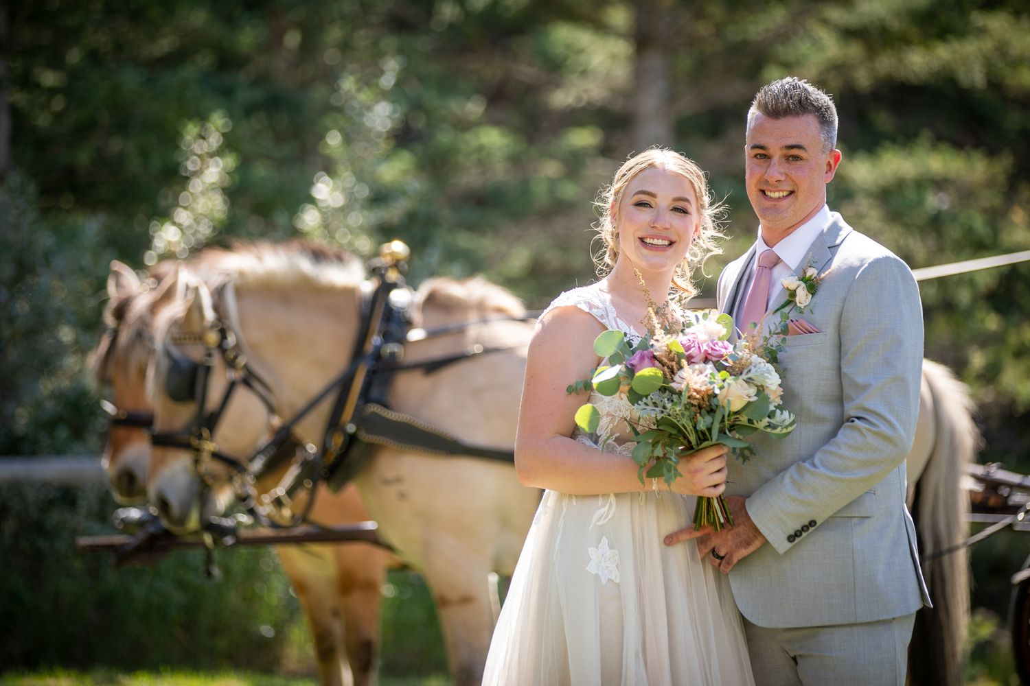 A couple poses together at their rustic outdoor wedding with a horse-drawn carriage in the background at Canmore ranch in Canmore, Alberta.