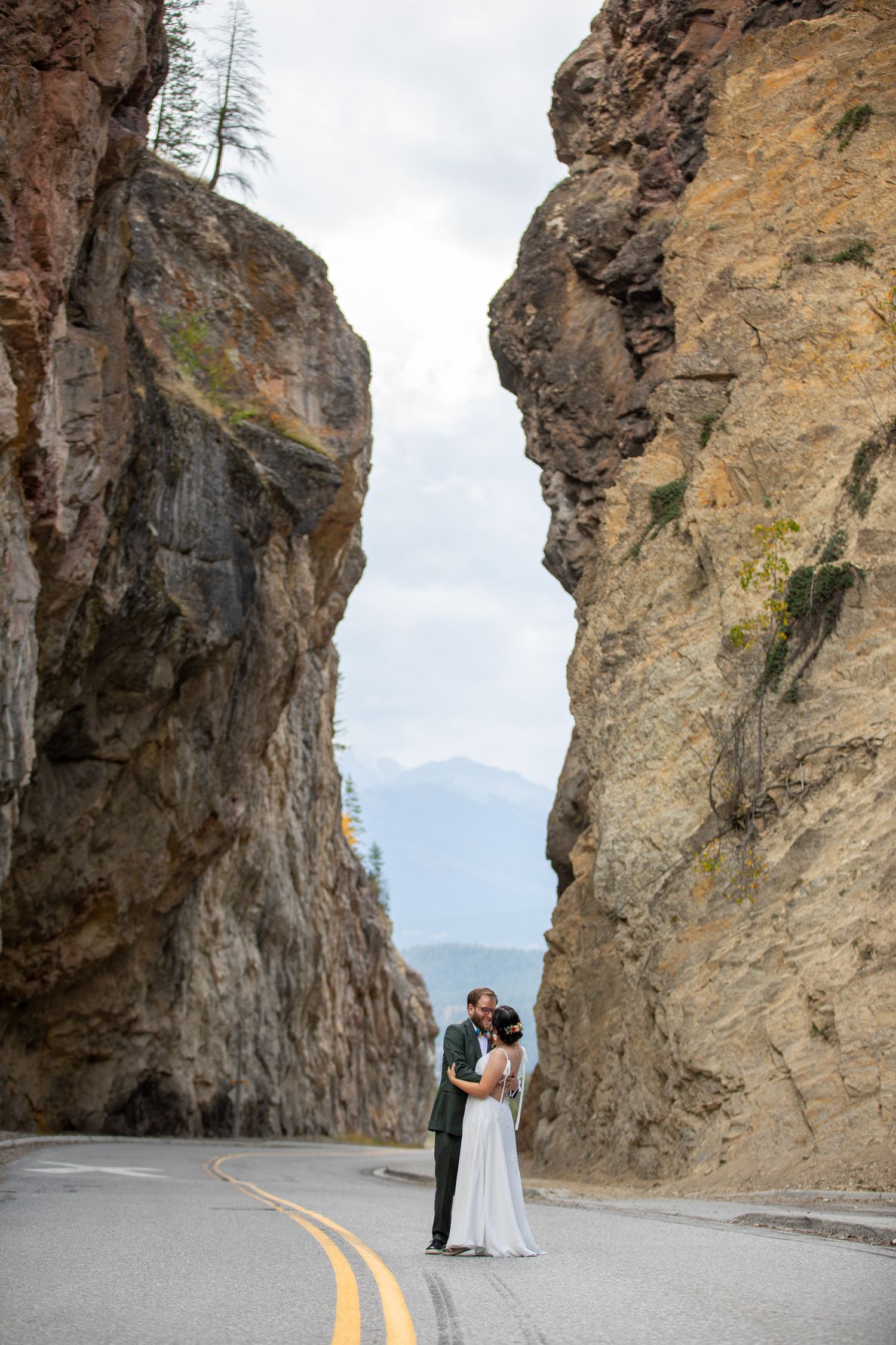 Wedding couple poses along scenic mountain road with dramatic rock formations of Sinclair Canyon in Radium, BC. Kootney National Park