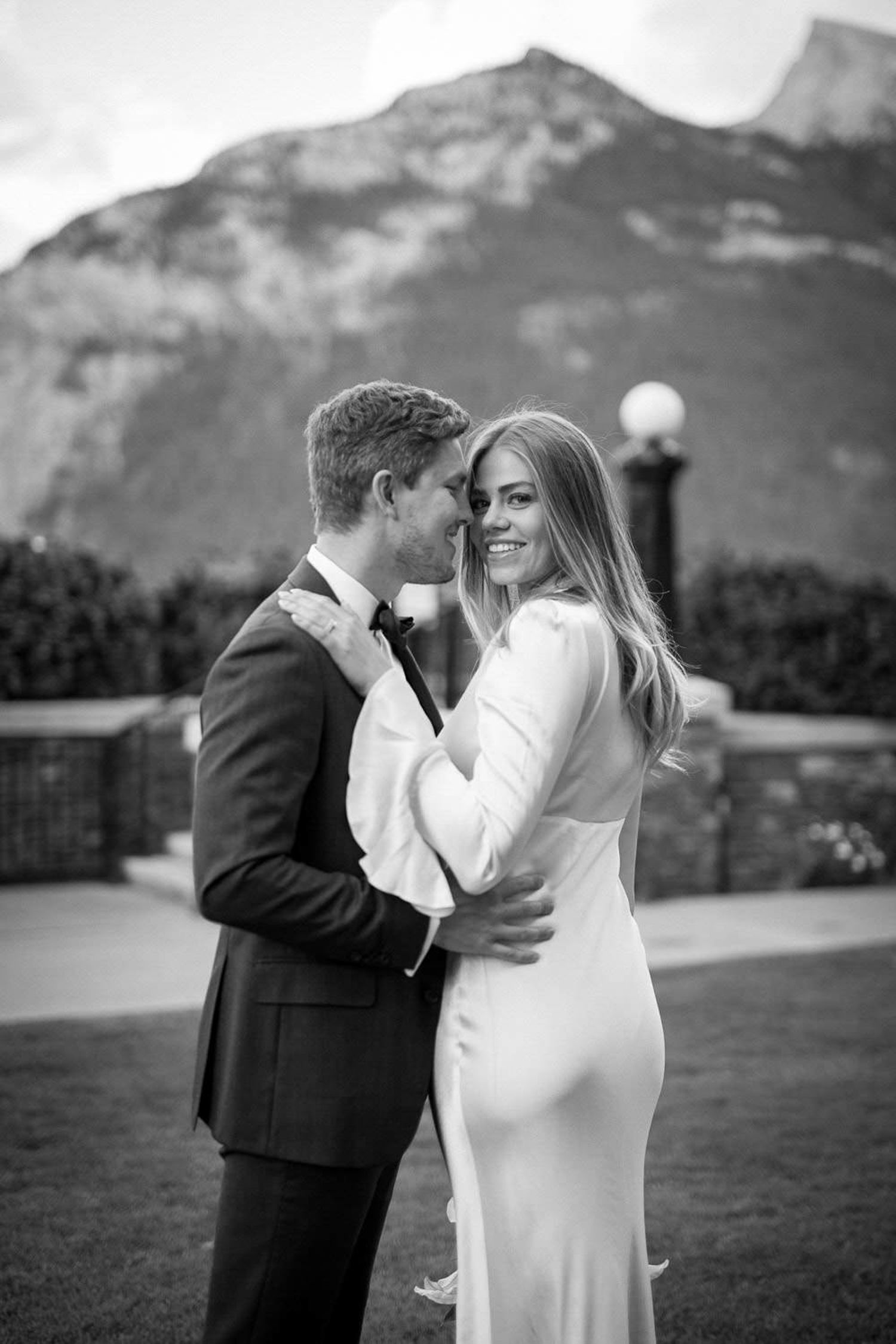 A romantic black and white wedding photo of a couple embracing  with a mountain backdrop at the Fairmont Banff Springs Hotel in Banff.