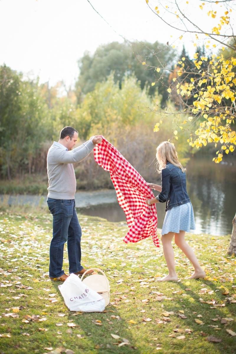 Couple spreading red checkered picnic blanket by a lake surrounded by autumn foliage at Fish Creek Park in Calgary.