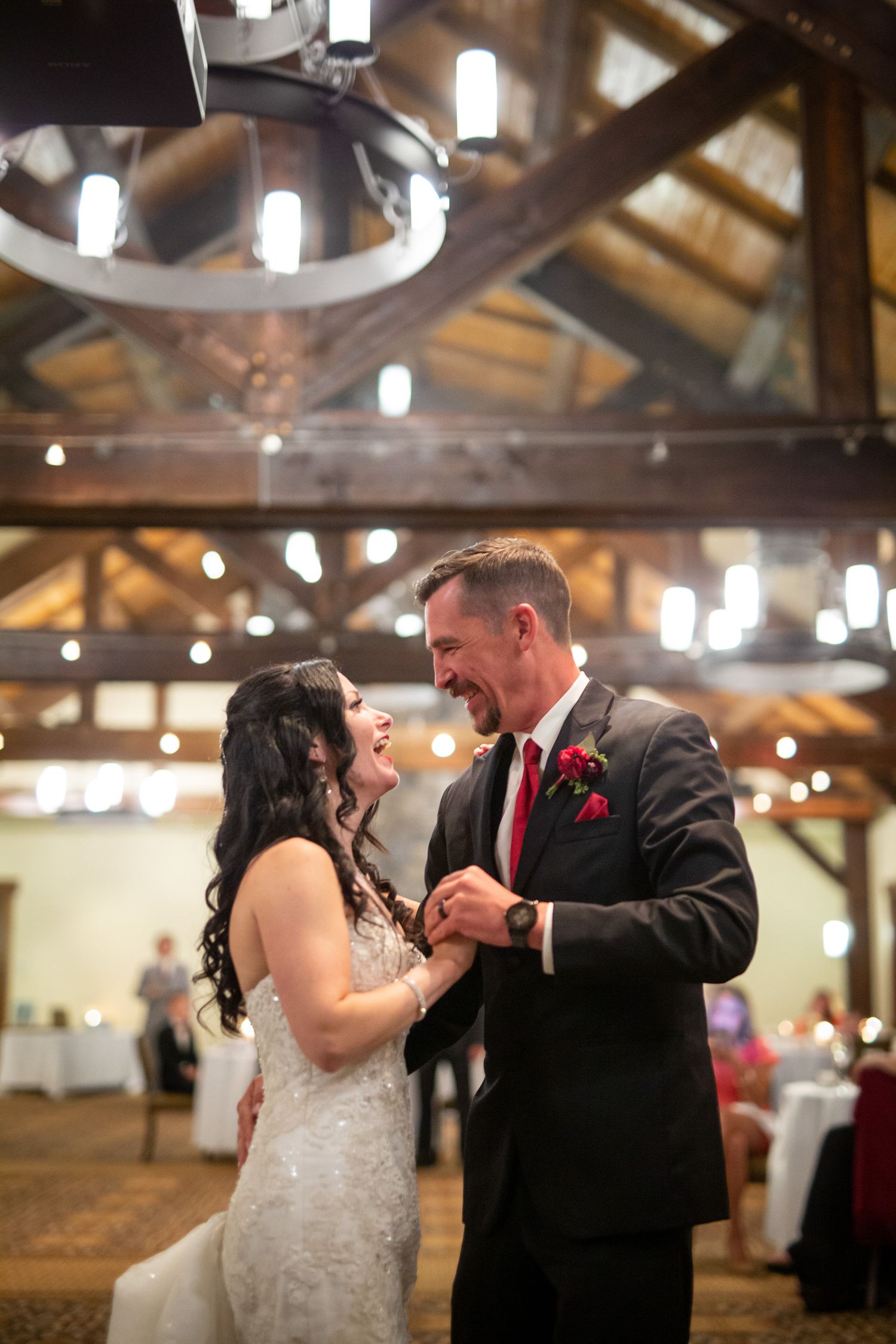 Bride and groom share joyful first dance at silvertip resort wedding venue with warm string lights and wooden beam ceiling.