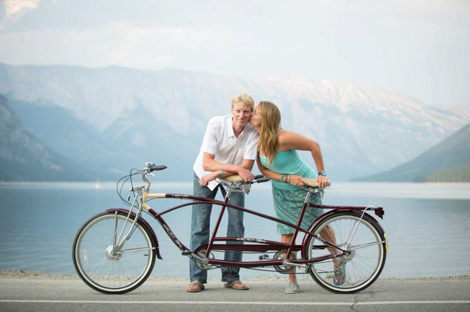A couple sits on a vintage bicycle against a scenic mountain lake Minnewanka in Banff National Park.
