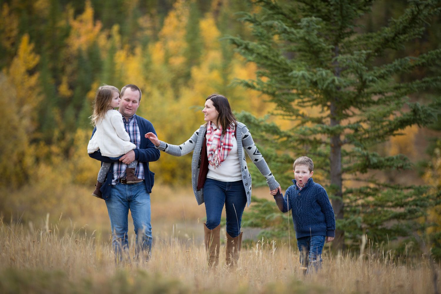 A family enjoys an autumn hike together through golden aspen trees and evergreen forest at Quarry Lake Park, Canmore, AB.