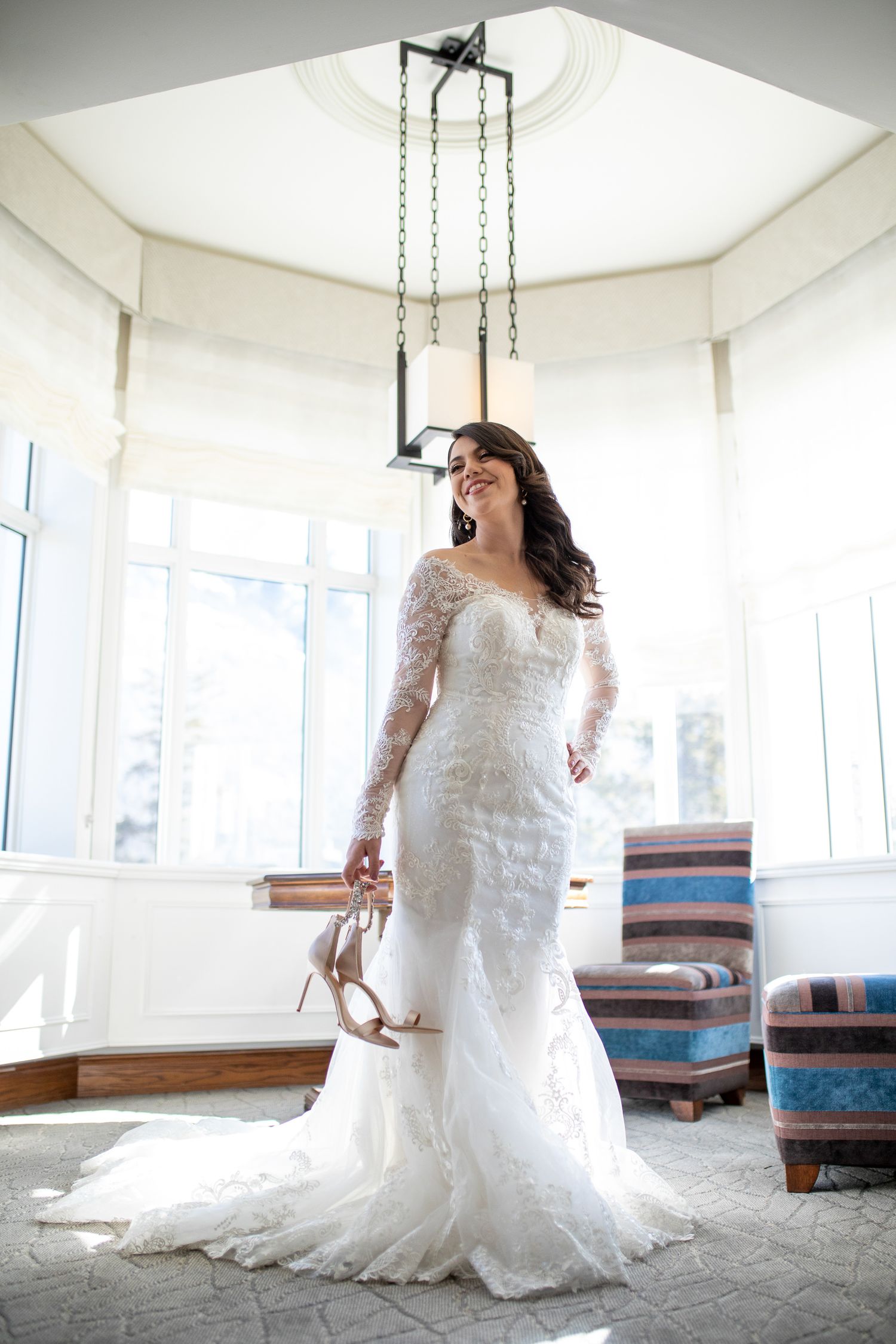 A bride in a white lace wedding dress poses gracefully in a bright sunlit room with rustic wooden benches. Fairmont Banff Springs Hotel