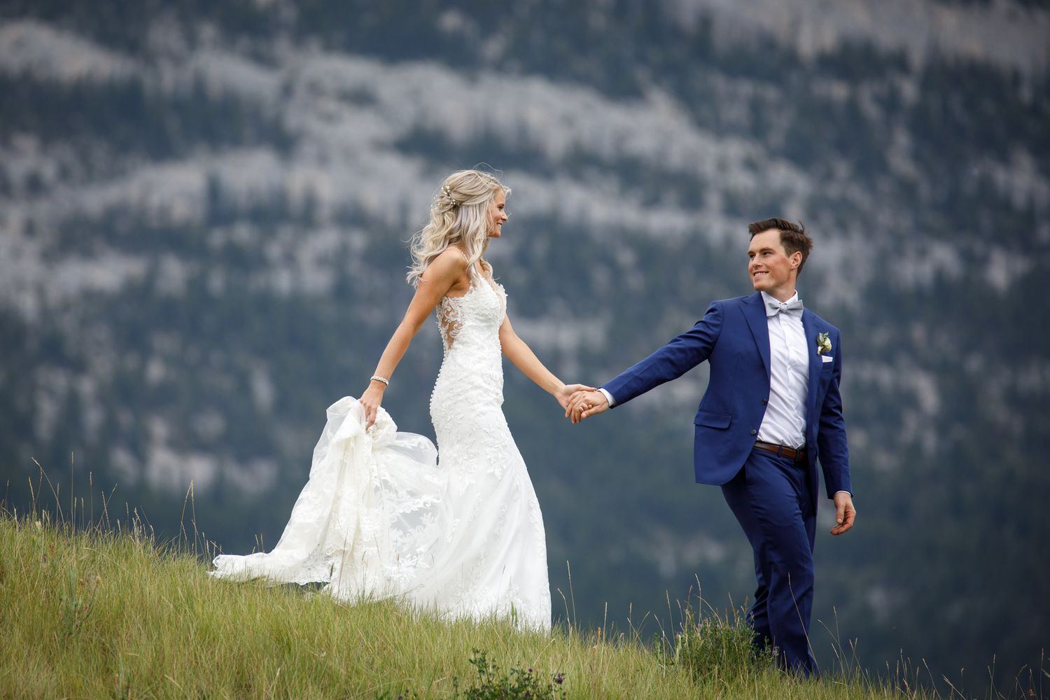 A couple in wedding attire dances playfully in a scenic mountain meadow on their special day. Canmore Three Sisters in Canmore, AB.