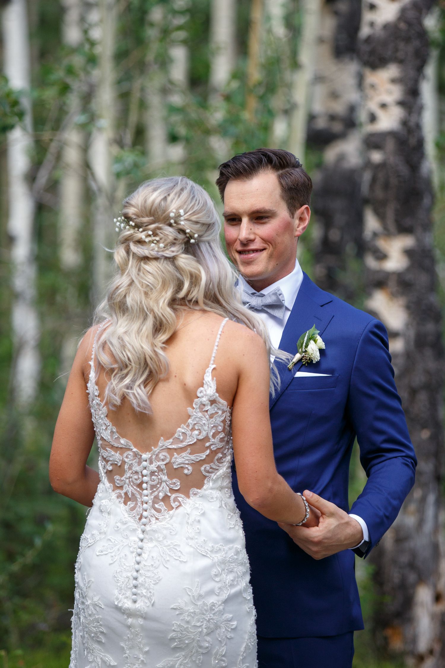A couple shares a romantic moment in a birch forest, with the bride wearing a detailed lace back wedding gown.