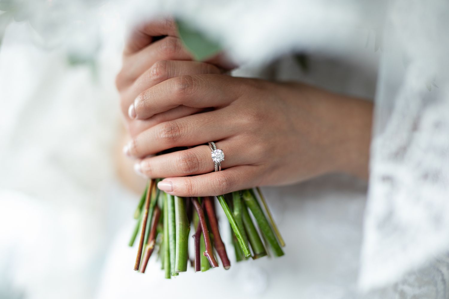 Bride holding a floral bouquet with a diamond engagement ring on her finger, close-up wedding photo.