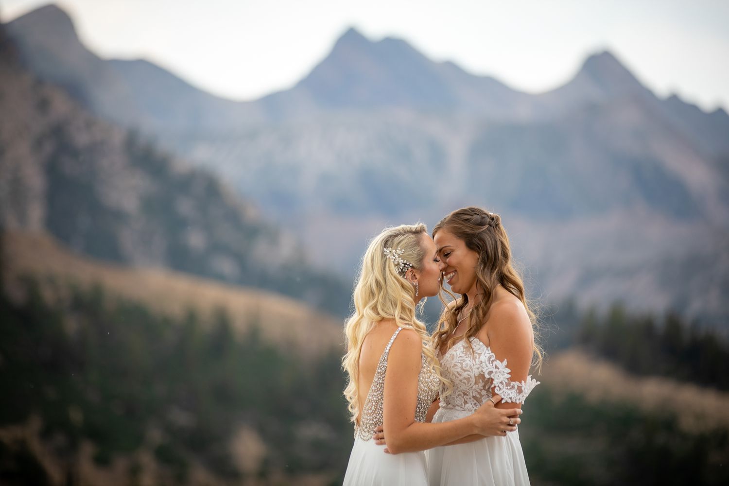 Two brides embrace in front of majestic mountain peaks during a wedding ceremony at sunset at Kicking Horse resort in Golden, BC