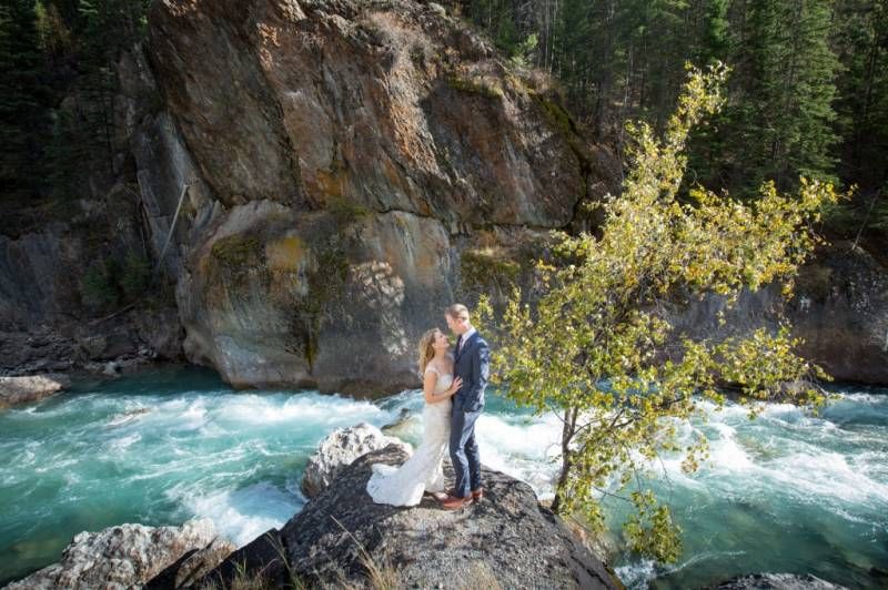 Bride and Groom on a rock by Toby creek river with turquoise waters rushing through rocky canyon at Panorama, BC.