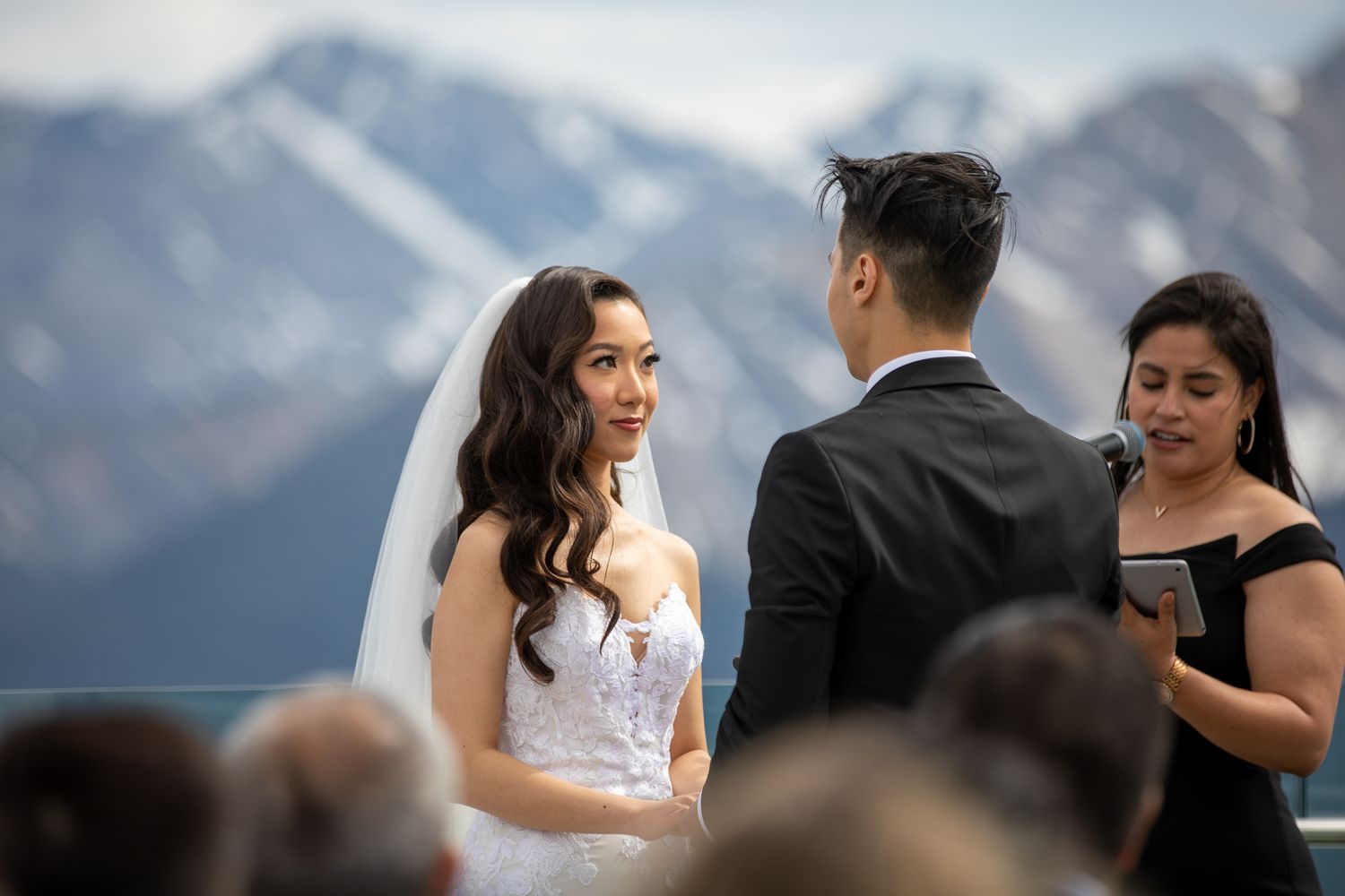 Bride and groom exchange vows at an outdoor mountain wedding ceremony with snow-capped peaks in the background.