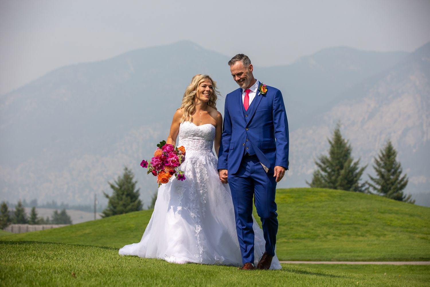 Bride and groom walking hand in hand on green golf course with mountain backdrop on their wedding day. Eagle Ranch Resort, BC.