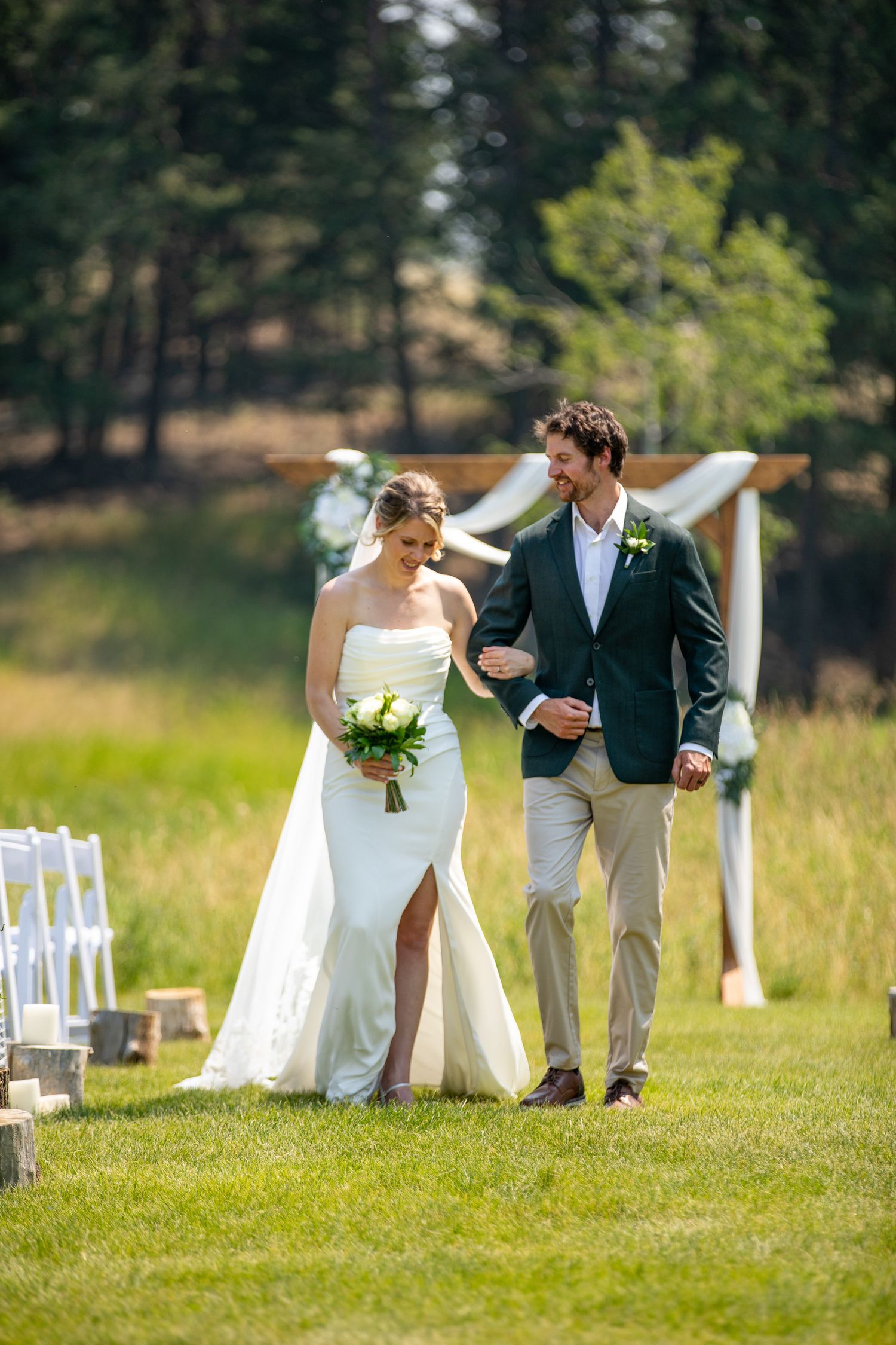 Bride and groom walking down outdoor aisle after wedding ceremony on green lawn with wooden arch backdrop at Swansea Ranch in Invermere, BC