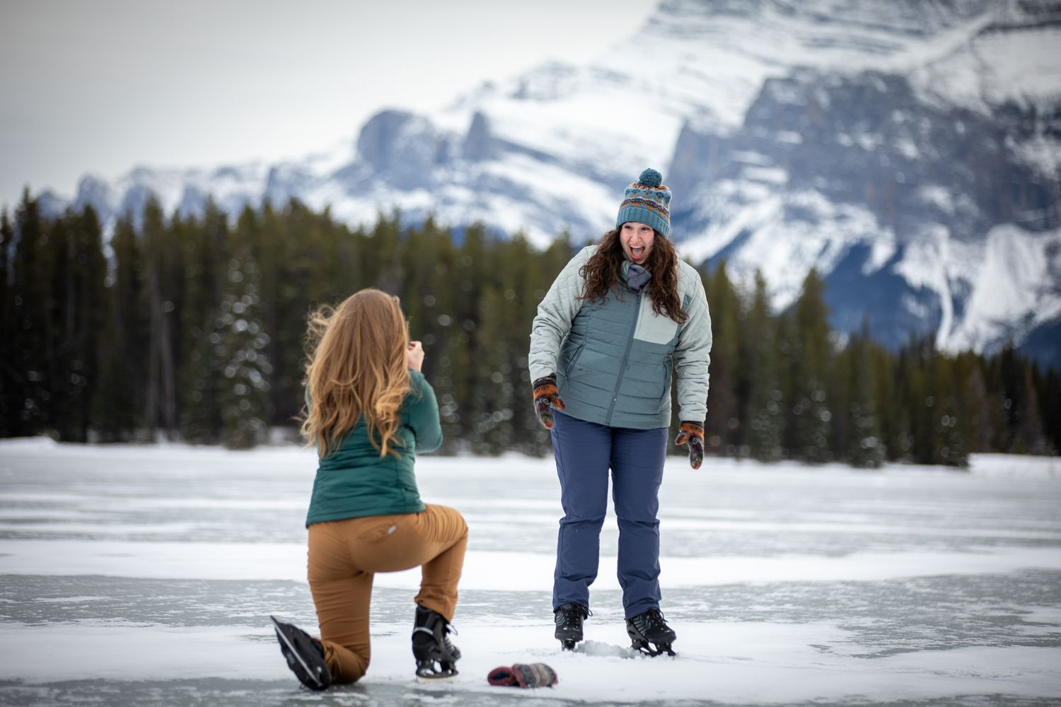A LGBTQ couple proposing at Two Jack Lake in Banff while skating on the lake in winter with Mount Rundle in background.