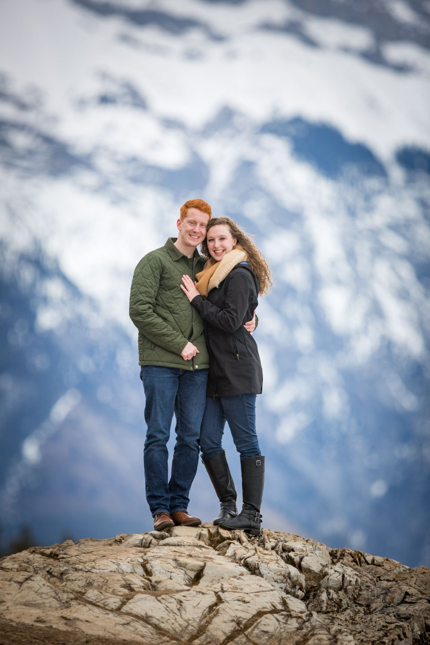 Couple embracing on a rocky summit with snow-capped mountains in the background at Lake Minnewanka in Banff National Park.