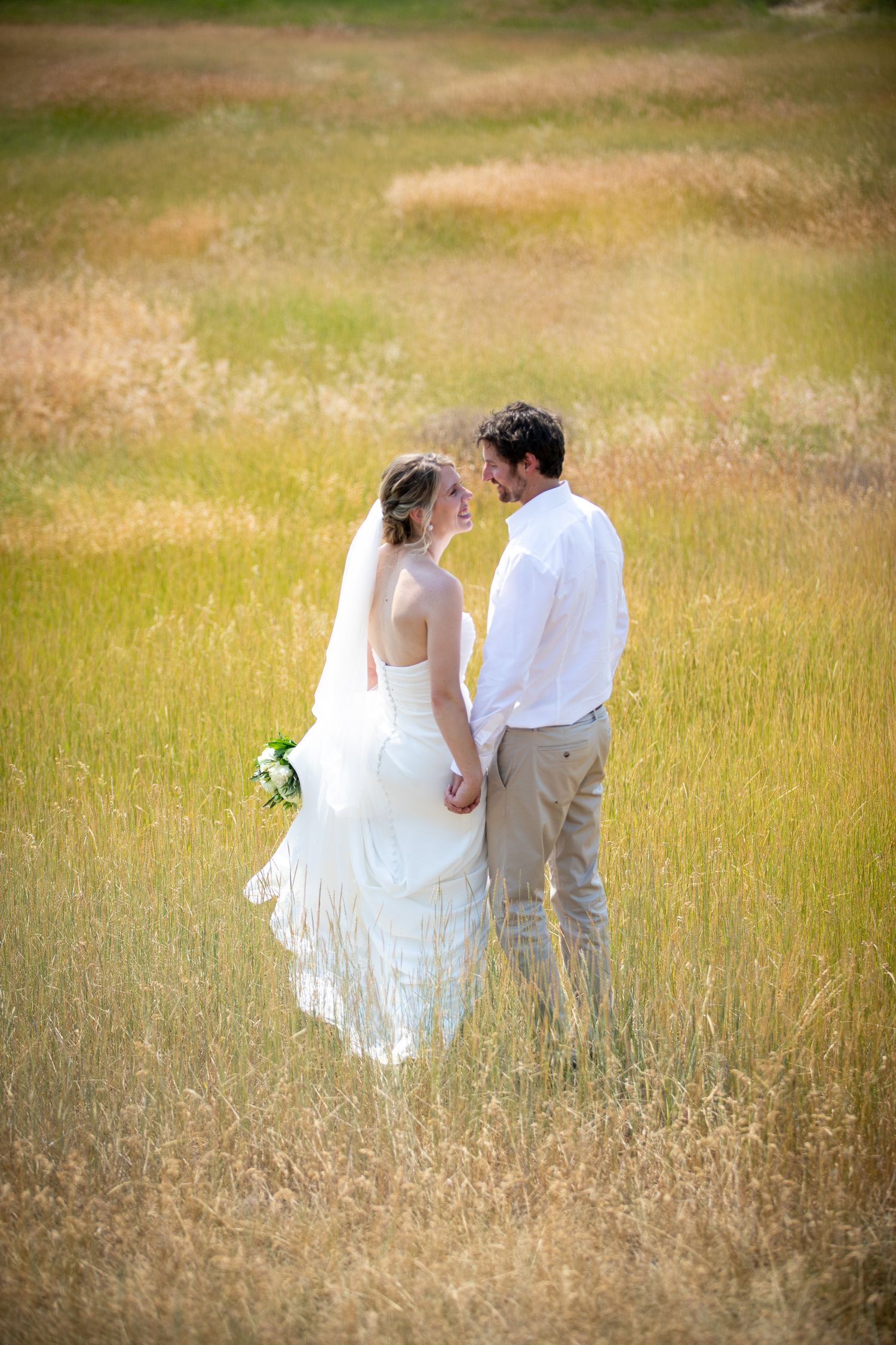 Bride and groom holding hands in golden field, sharing intimate moment in wedding attire at Swansea Ranch in Invermere, BC
