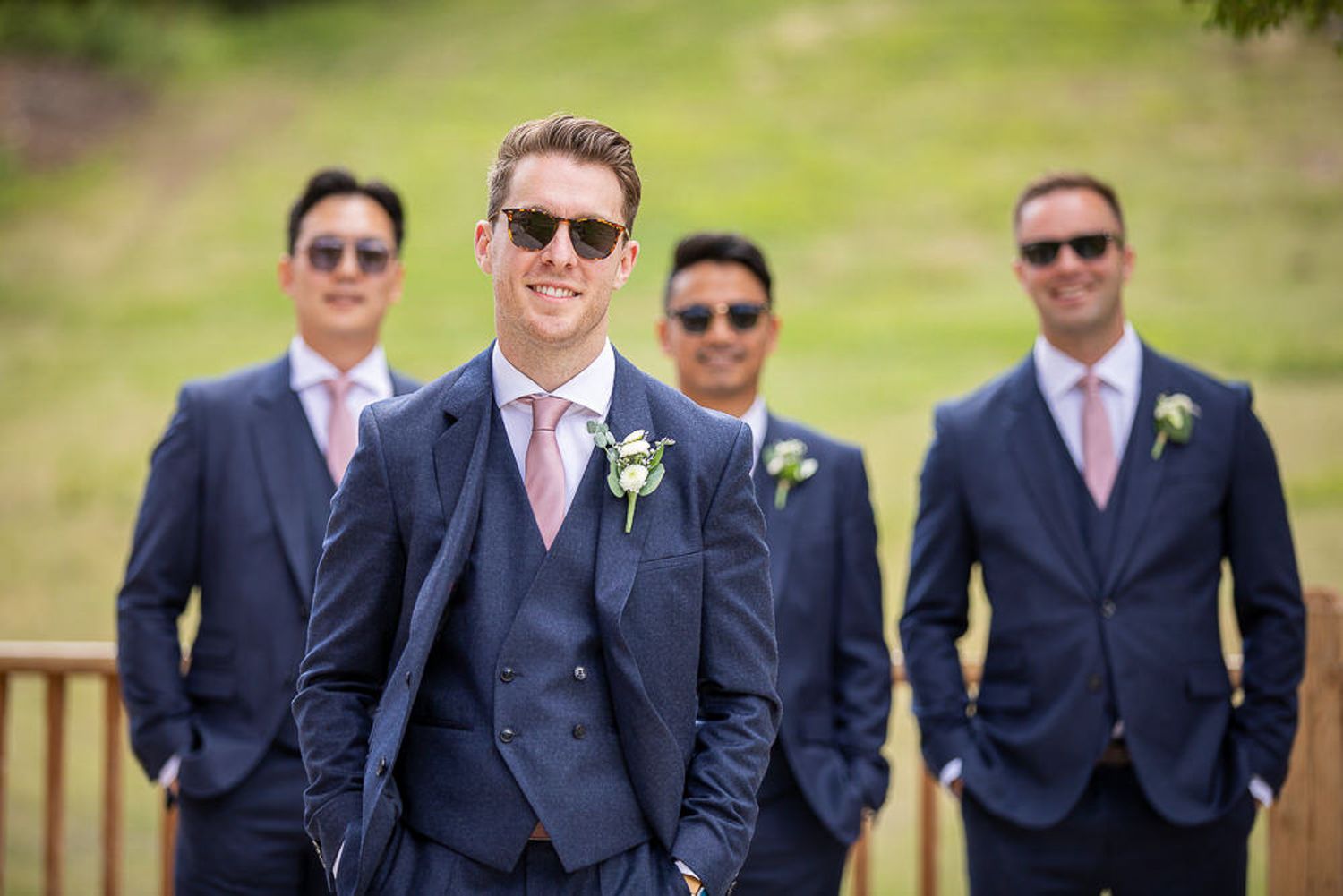 Wedding party wearing navy suits and sunglasses pose together outdoors on a sunny day. Mount Norquay resort, Banff.