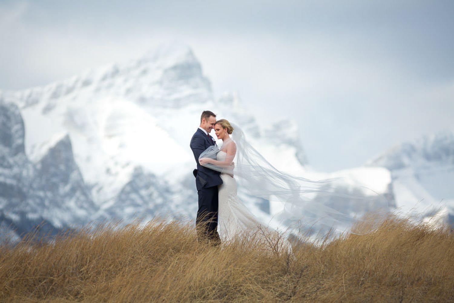 Romantic wedding couple embraces against stunning snow-capped mountain backdrop in scenic landscape. Canmore Three Sisters.