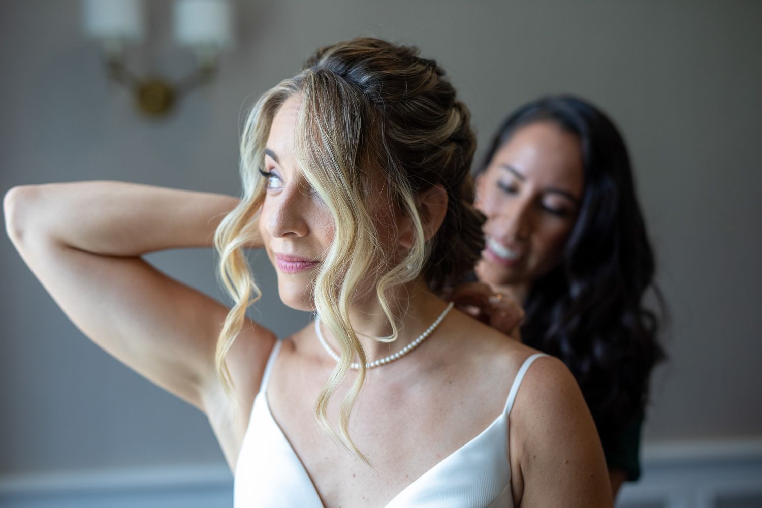 Two women getting ready together, with one helping style the other's hair in soft indoor lighting. Fairmont Chateau Lake Louise, AB