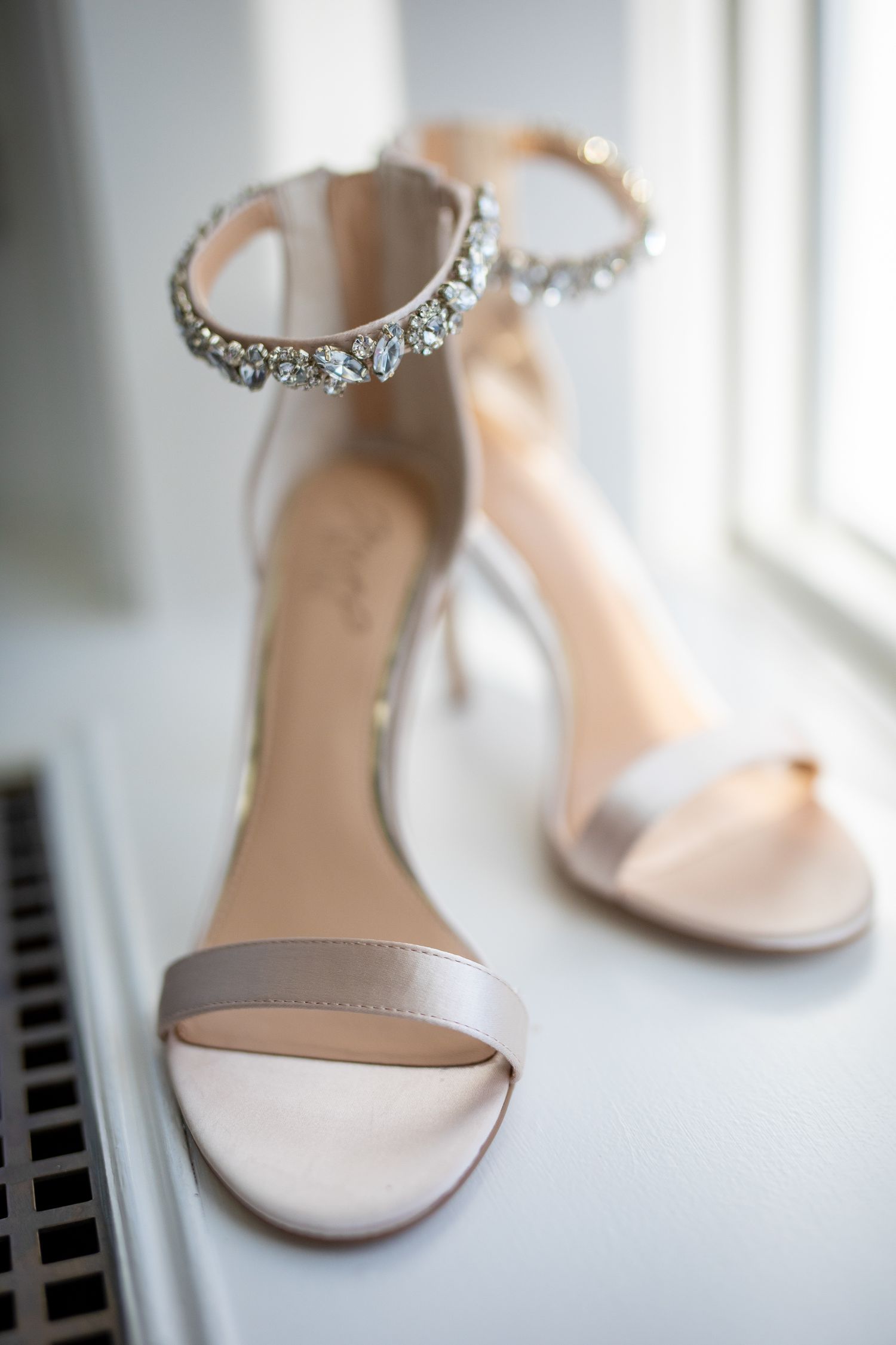 Elegant white satin bridal sandals with crystal-embellished ankle straps displayed in soft window light.Fairmont Banff Springs Hotel