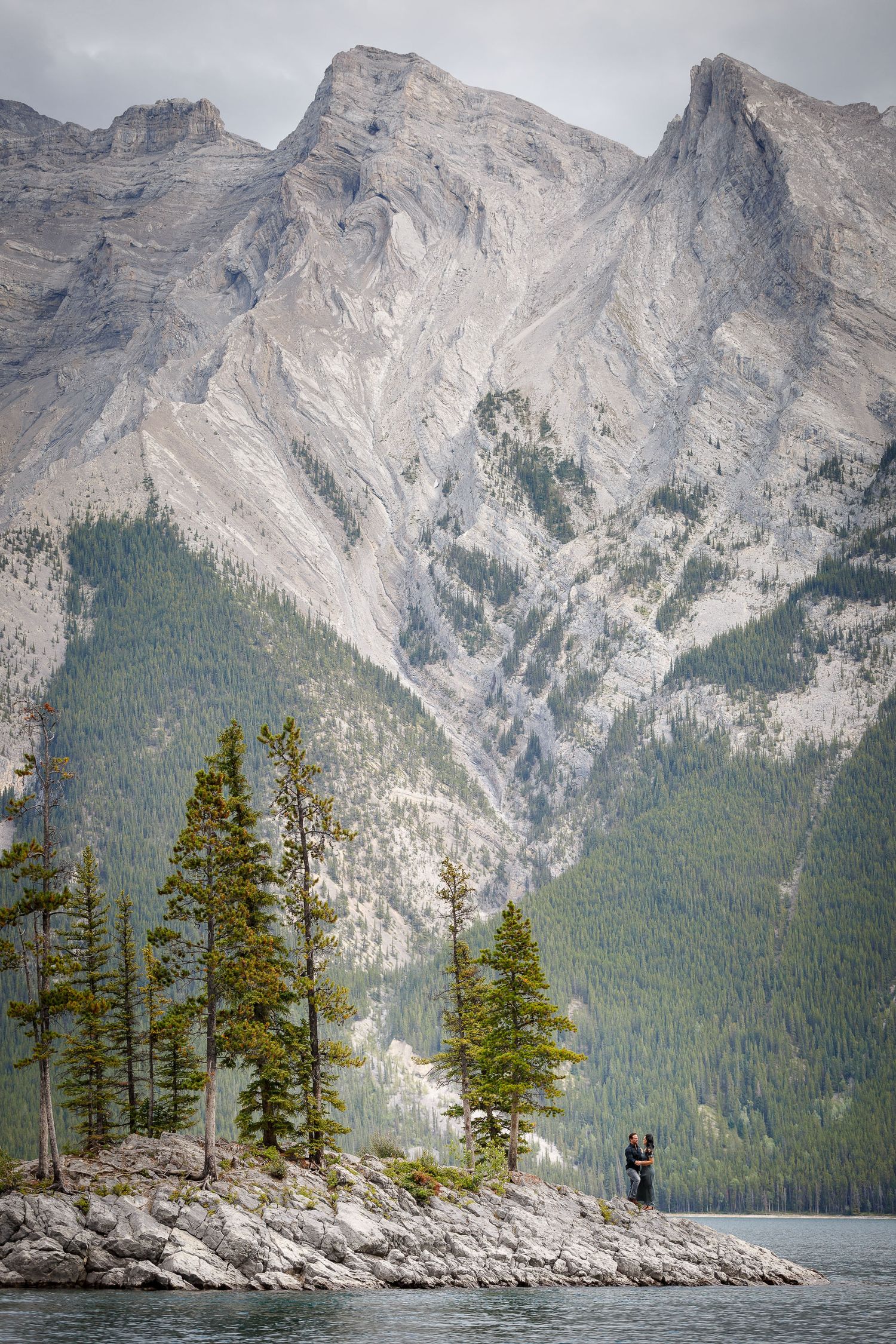 A scenic landscape with majestic mountains, pine forests, and a tranquil lake in the foreground at Lake Minnewanka in Banff.