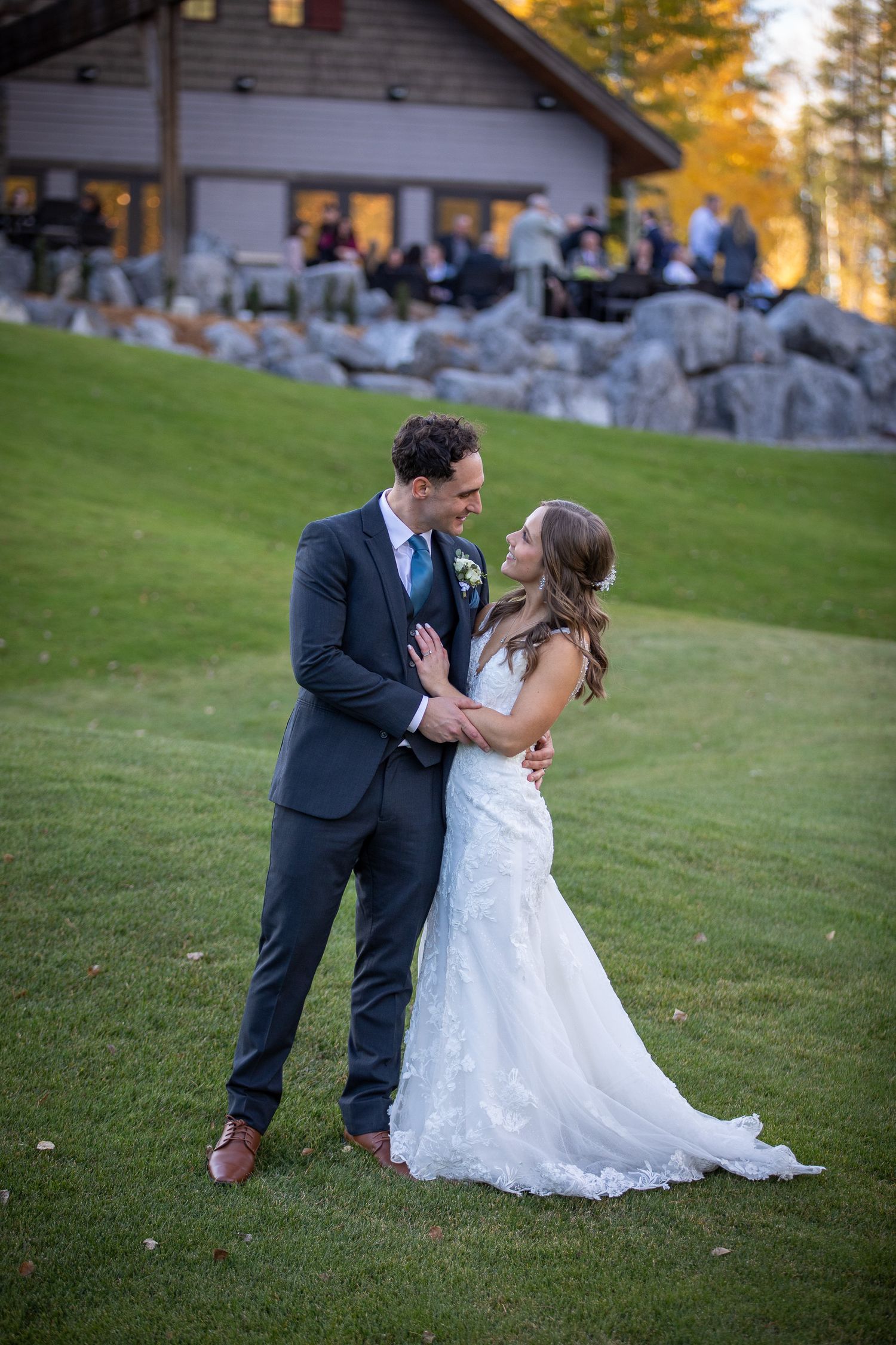 A couple in wedding attire shares a romantic moment on a grassy hillside during golden hour at Silvertip resort in Canmore, AB