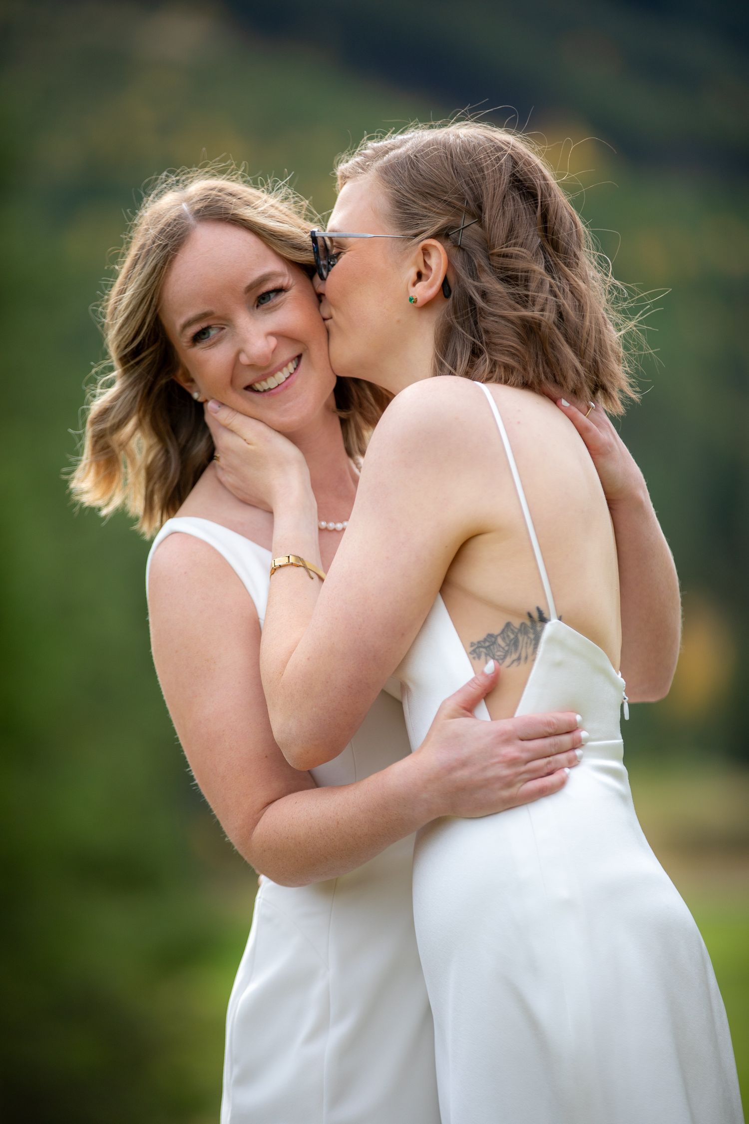 A LGBTQ couple in white dresses share an intimate embrace outdoors against a blurred natural background Panorama Mountain Resort.