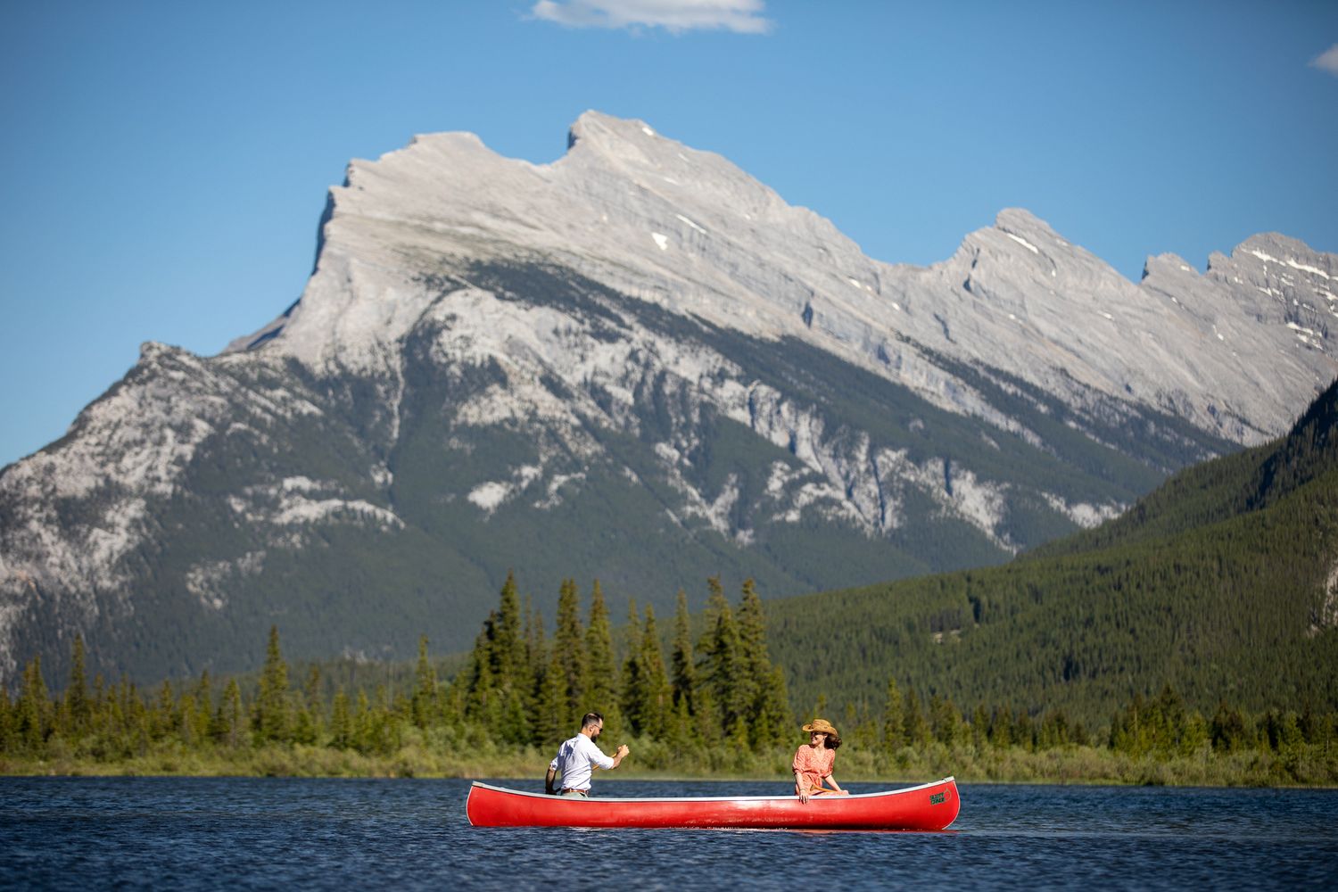 A red canoe glides across calm waters with majestic Rocky Mountains rising in the background at Vermilion Lakes.